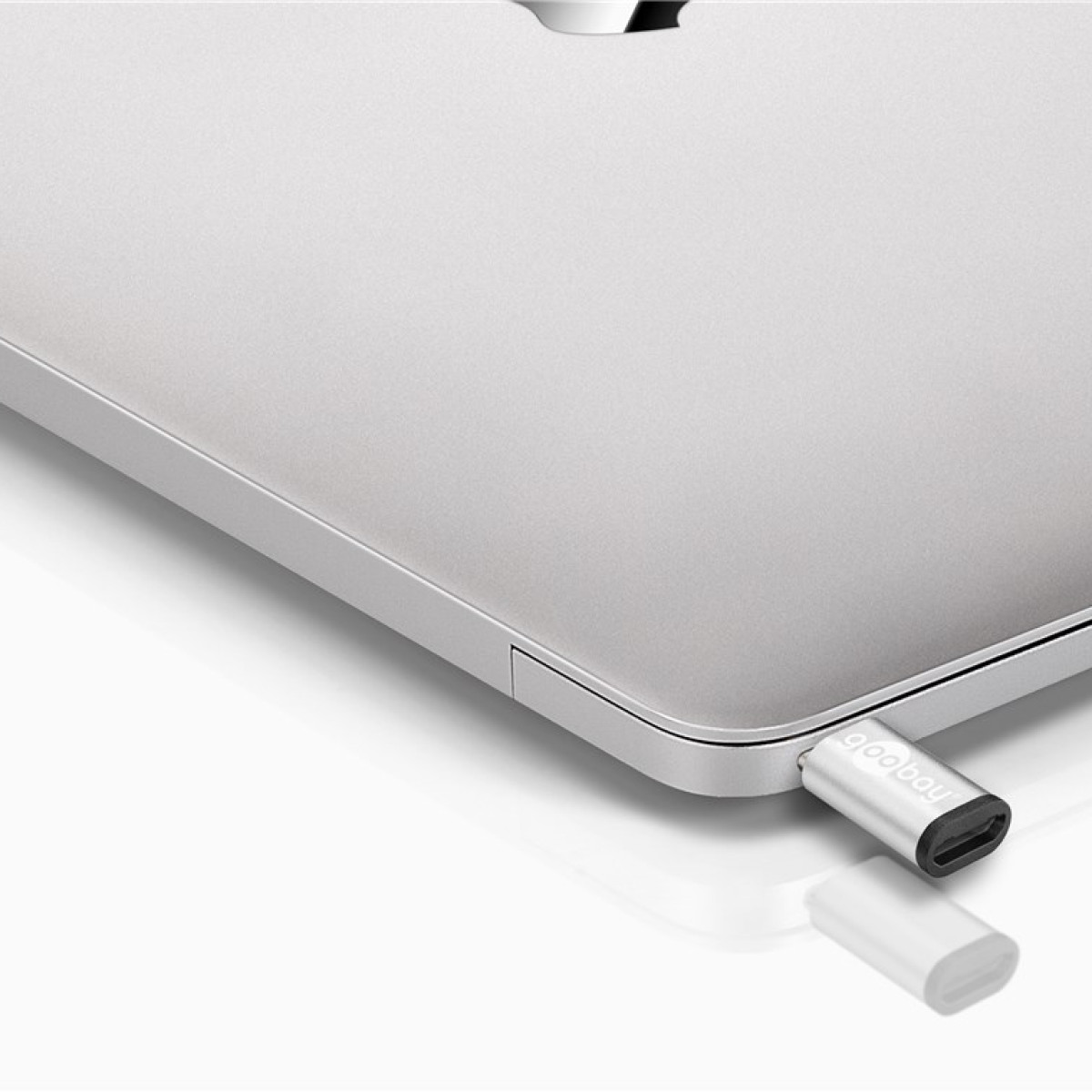 Srebrny adapter USB-C jest podłączony do laptopa. Obok leży biały adapter.