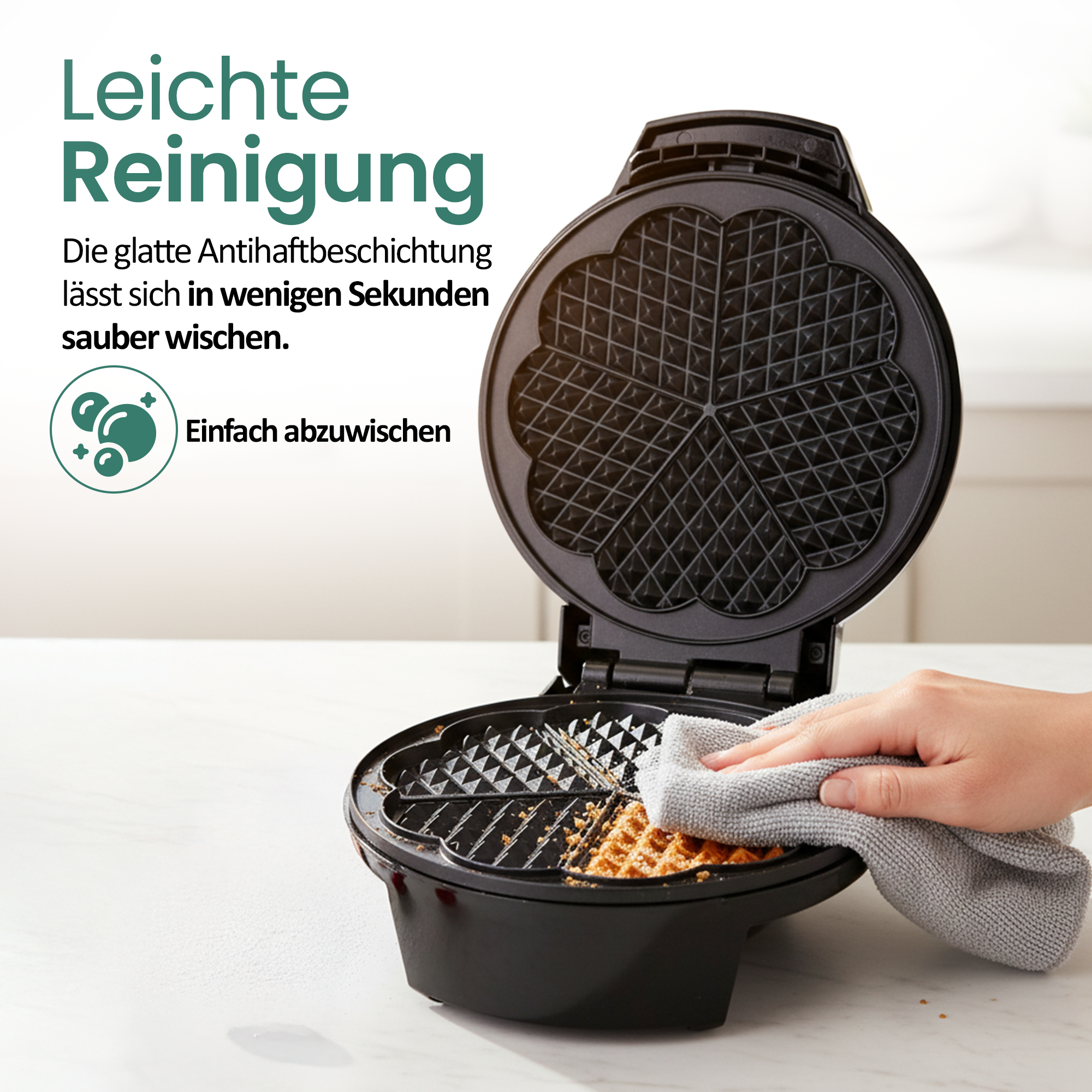 Eine Hand wischt eine Herz-Waffelform mit einem grauen Tuch ab.