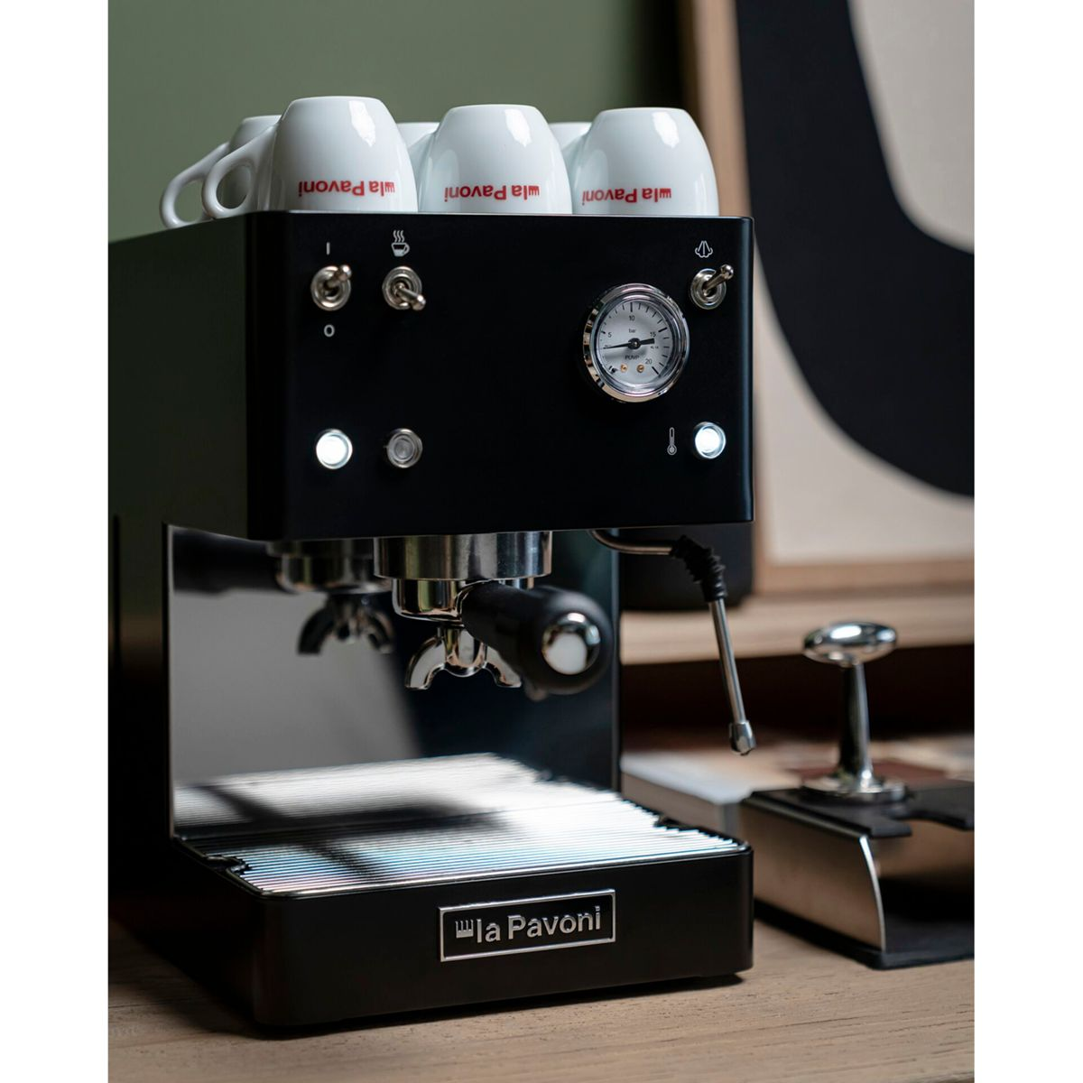 Schwarze Espressomaschine mit vier weißen Tassen oben, Druckanzeige und Hebel.