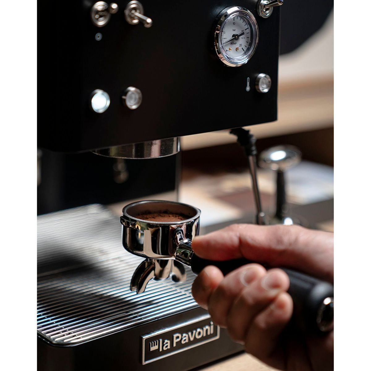 Eine Hand hält den Siebträger einer Espressomaschine mit Kaffeepulver.