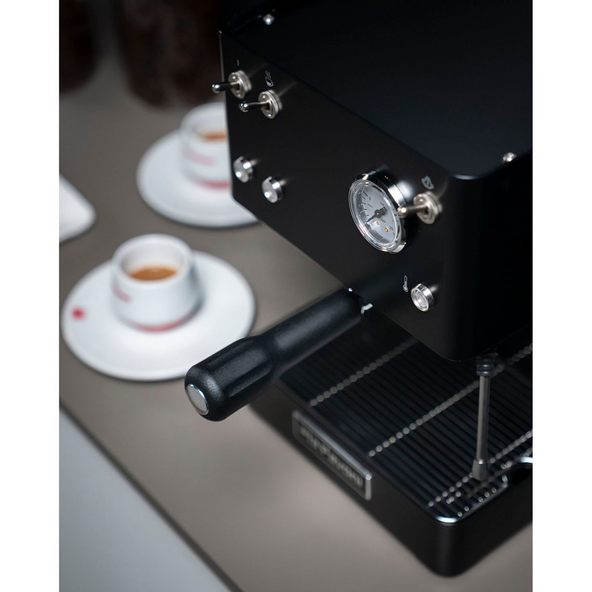 Schwarze Espressomaschine mit Manometer, zwei Espressotassen und Griff.