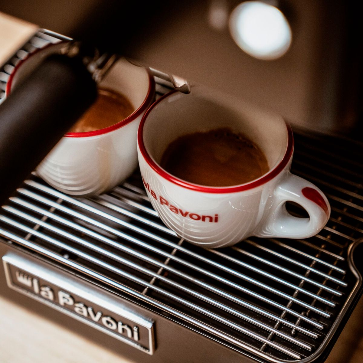Zwei weiße Espressotassen mit rotem Rand auf einer Kaffeemaschine.