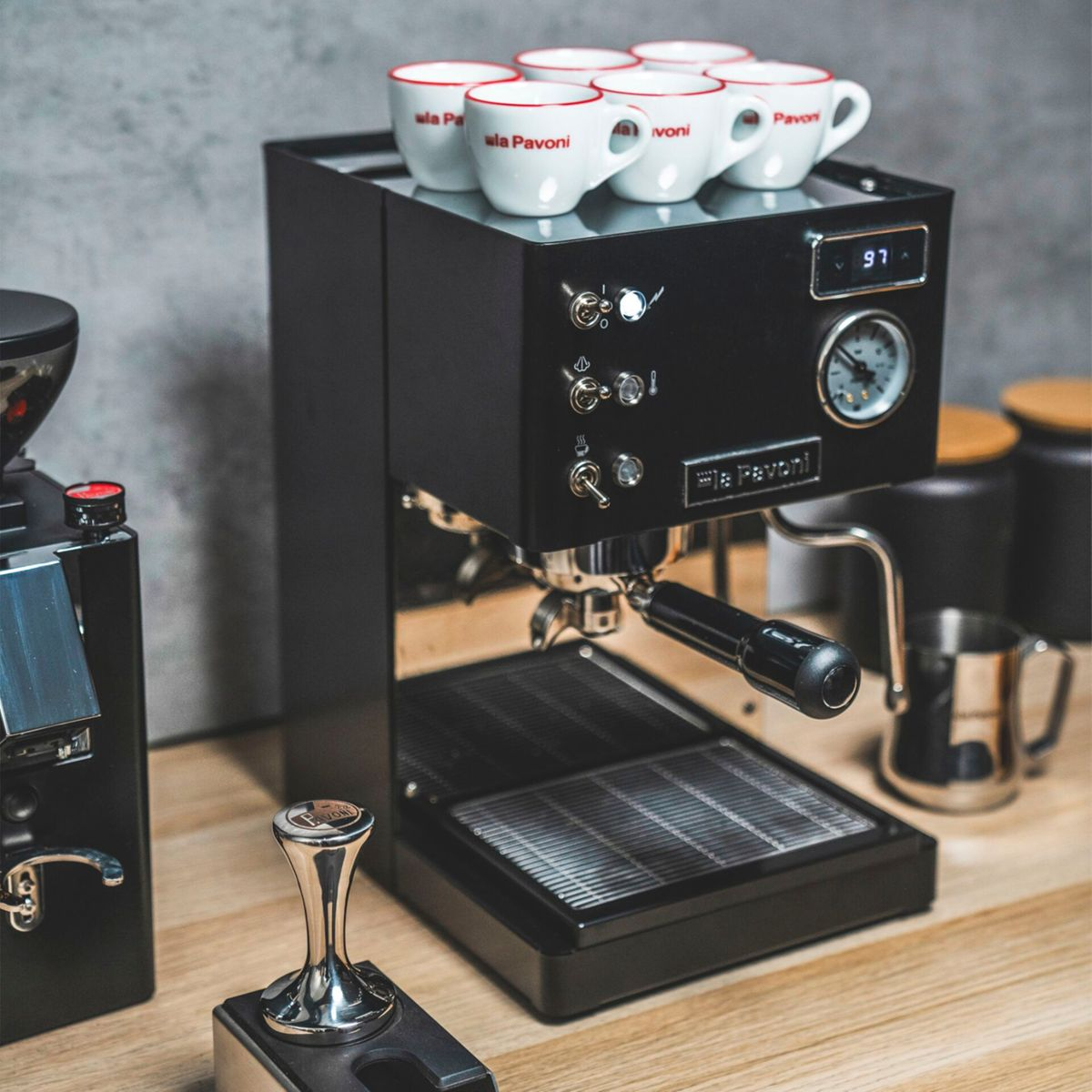 Eine schwarze Espressomaschine mit vier Tassen auf der Oberseite, daneben eine Kaffeemühle.