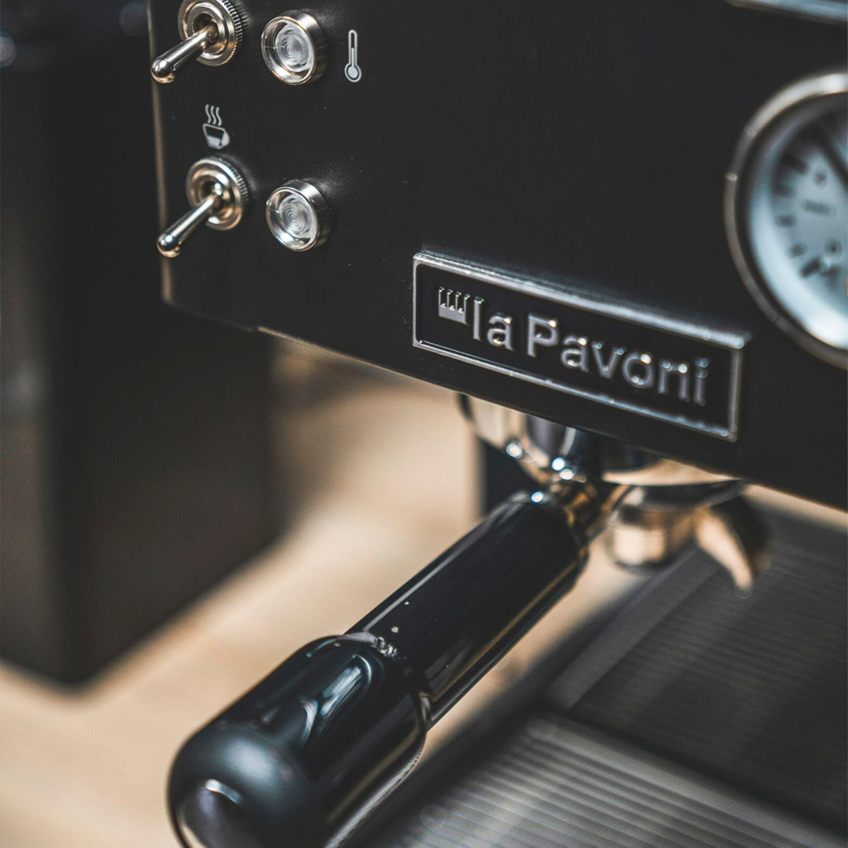 Nahaufnahme einer schwarzen Espressomaschine mit Schalter und Thermometeranzeige.