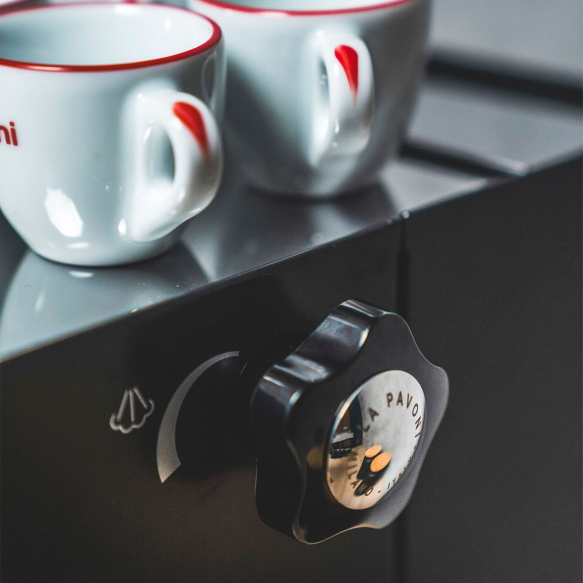 Zwei weiße Espressotassen mit rotem Rand auf einer Kaffeemaschine.