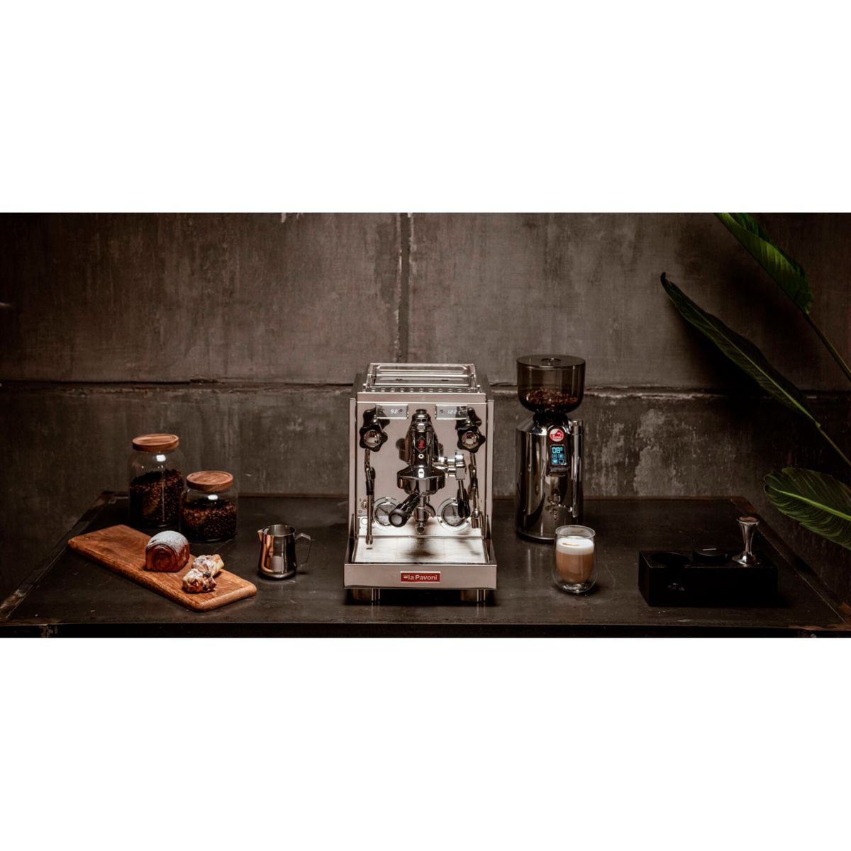 Espressomaschine, Mühle, Gebäck und Kaffee auf einem Tisch.