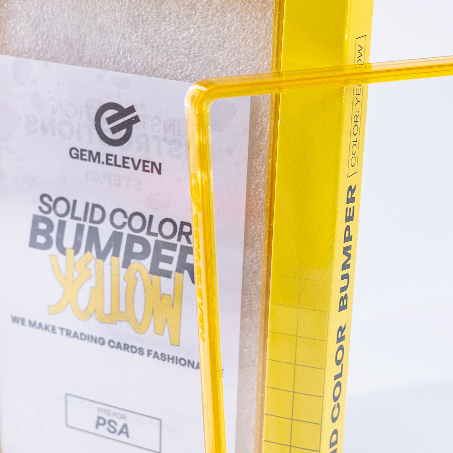 Gelber Schutzrahmen für Sammelkarten mit Aufdruck „GEM.ELEVEN“ und „SOLID COLOR BUMPER“.
