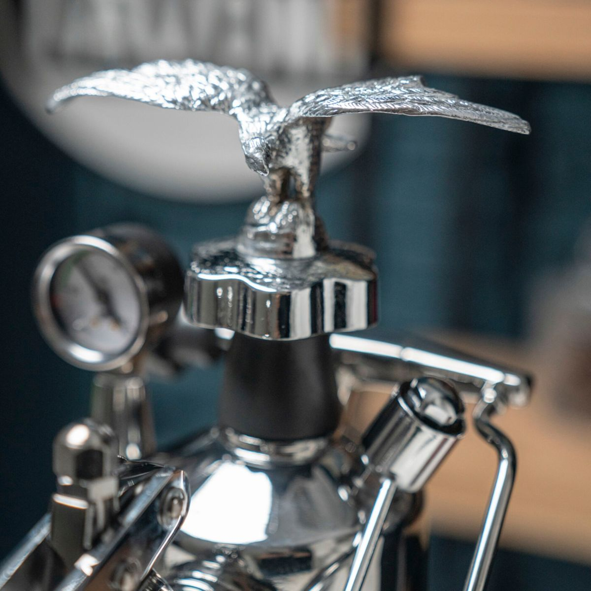 Eine glänzende silberne Adlerfigur thront auf einer Espressomaschine mit Manometer.
