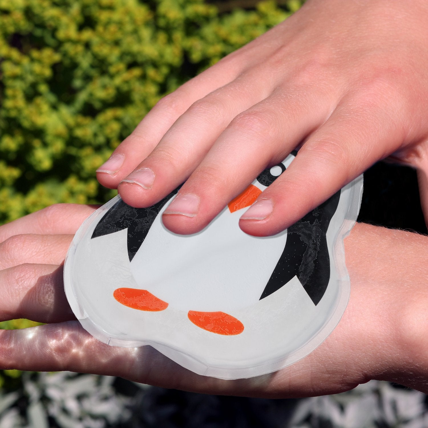 Manos sosteniendo una bolsa de agua caliente transparente con diseño de pingüino.