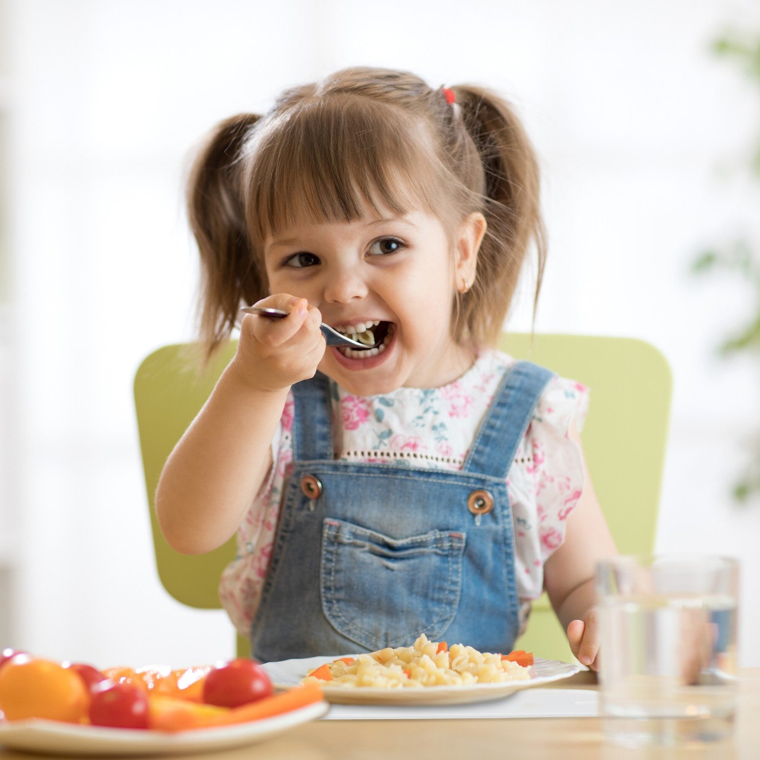 Una niña come pasta con un tenedor en una mesa.