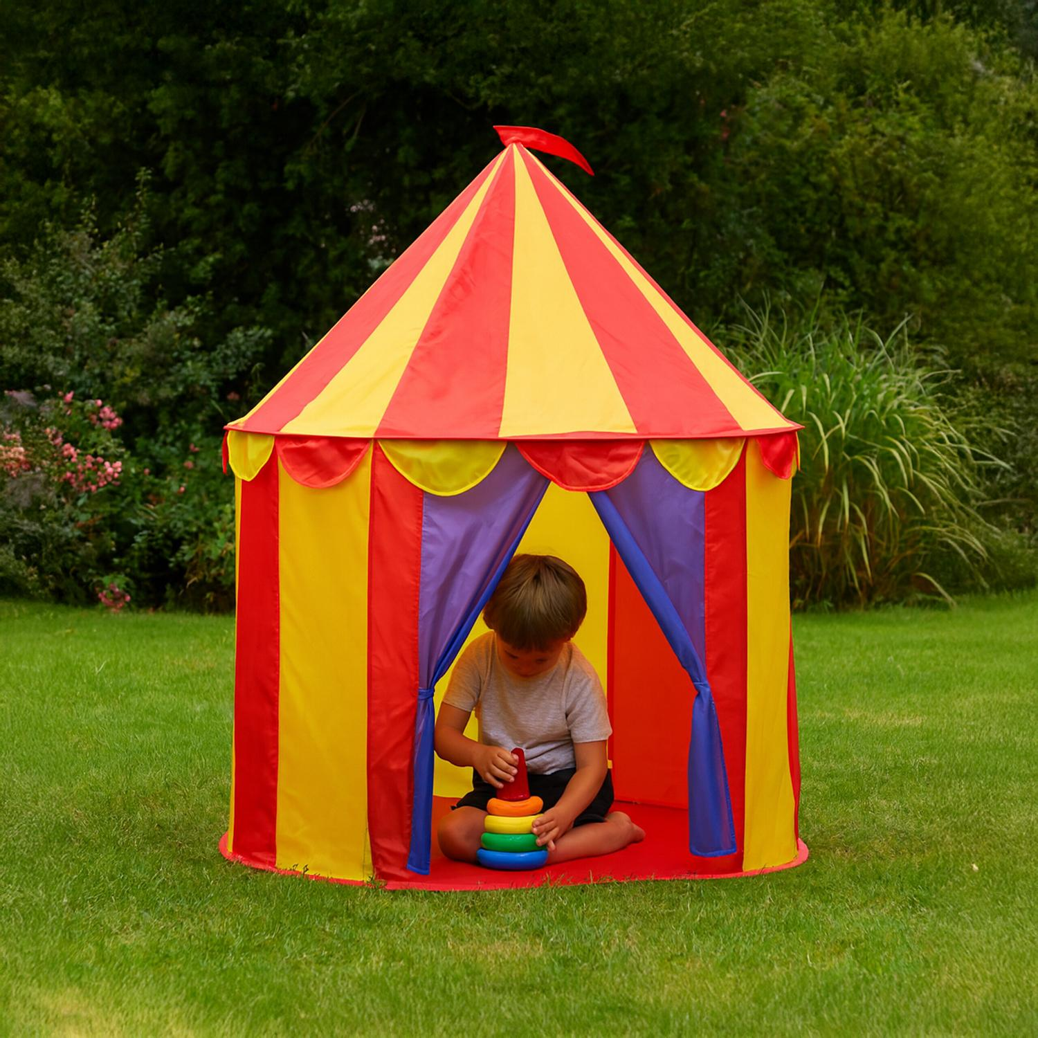 Un niño juega con un juguete de anillos apilables dentro de una carpa de circo colorida.