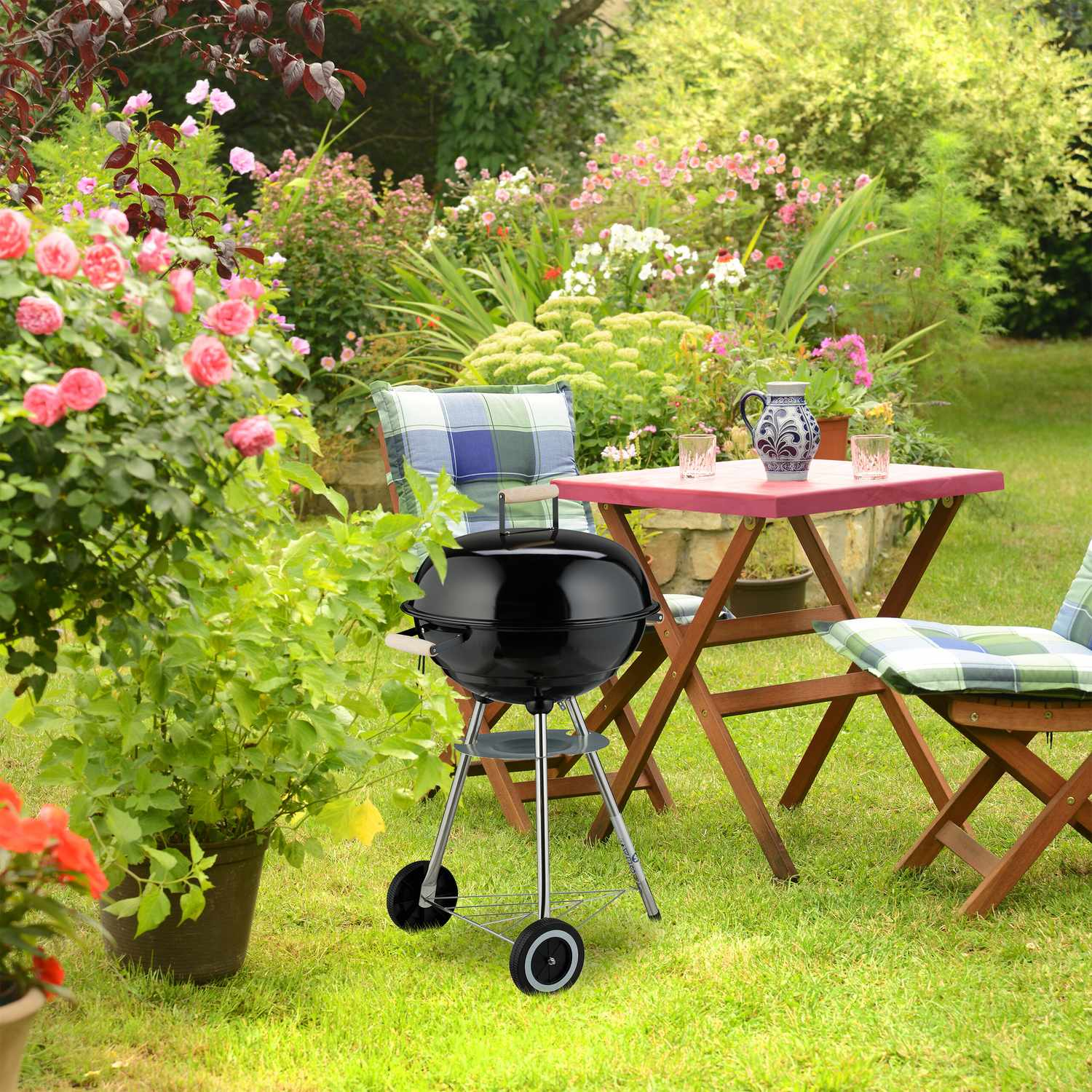 Una parrilla negra sobre césped frente a mesa con sillas y flores.