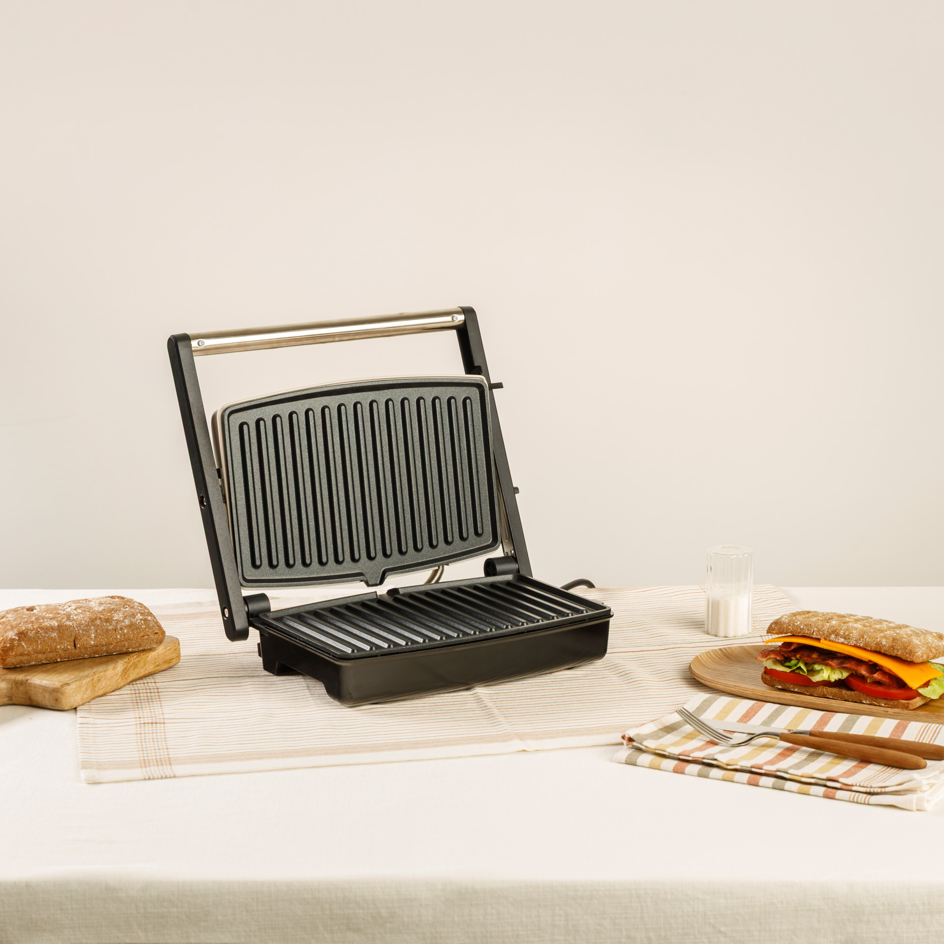 Una sandwichera abierta con pan y un sándwich al lado.
