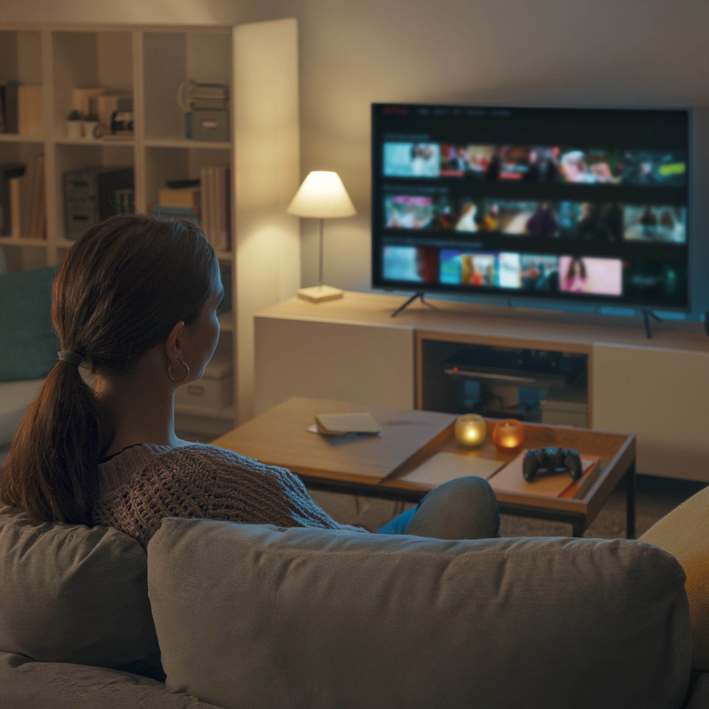 Kobieta siedzi na kanapie, ogląda stronę główną Netflix na TV.