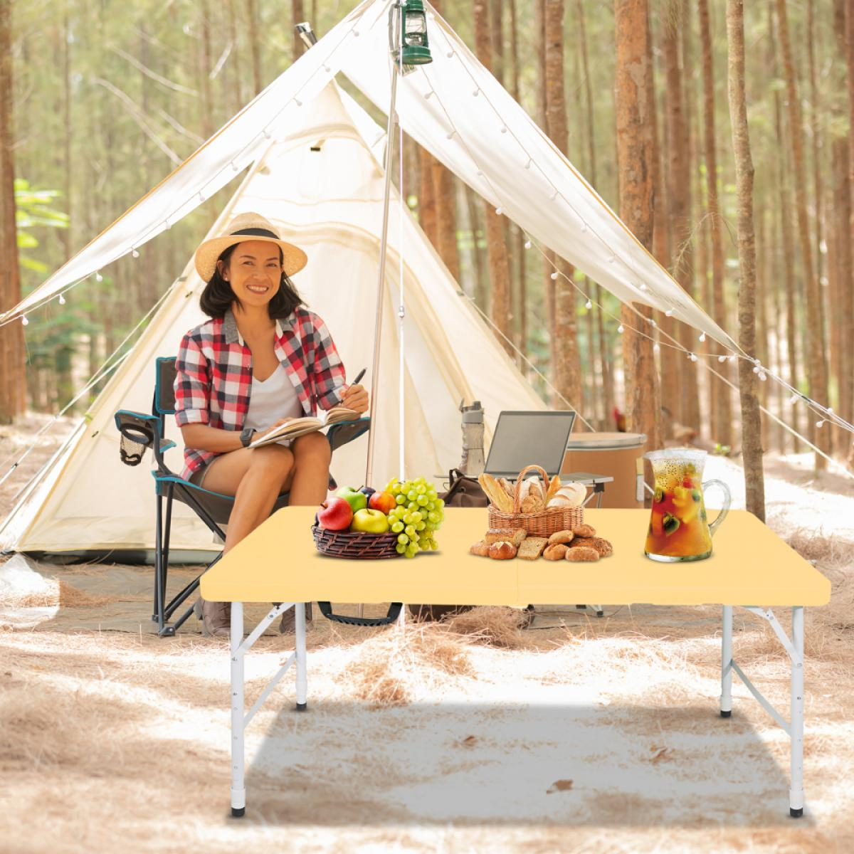 Frau beim Camping, schreibt im Notizbuch am Zelt. Tisch mit Obst, Brot und Getränk.