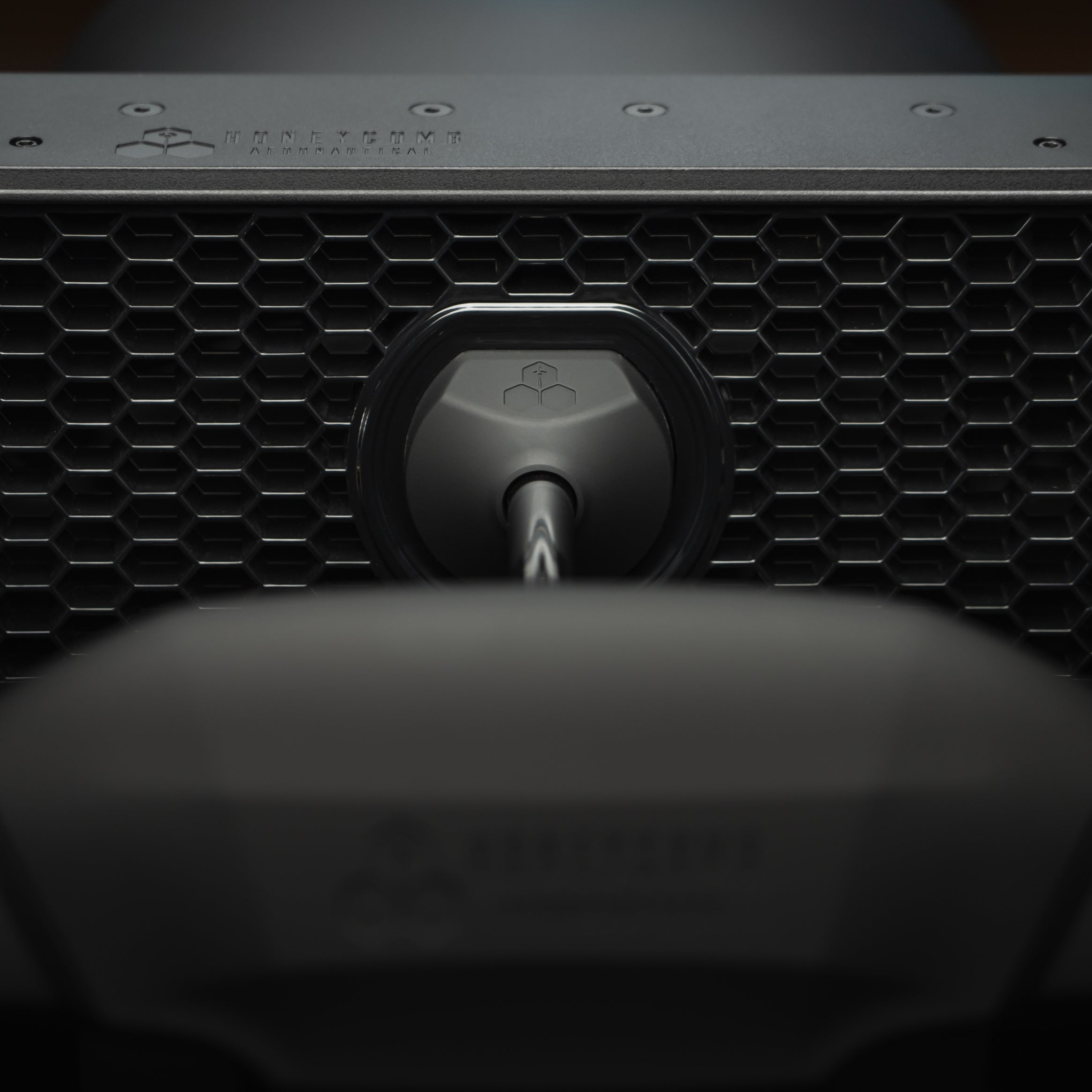 Close-up of a black hexagonal grill with a central emblem and a rod.