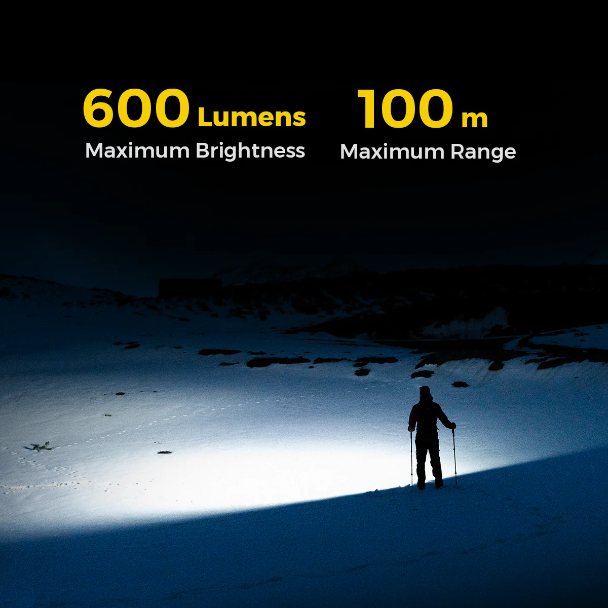 Ein Mensch mit Stöcken steht in der Nacht in einer verschneiten Landschaft unter einem Lichtkegel.