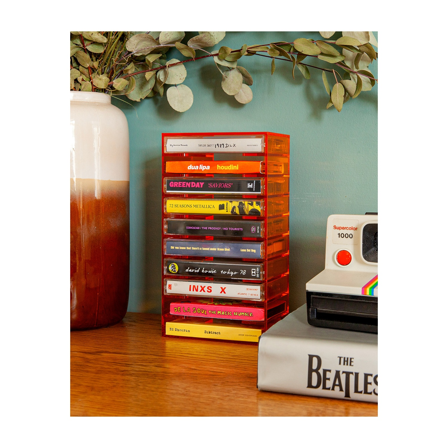 Support de cassettes orange avec cassettes de musique, appareil photo Polaroid et livre des Beatles.