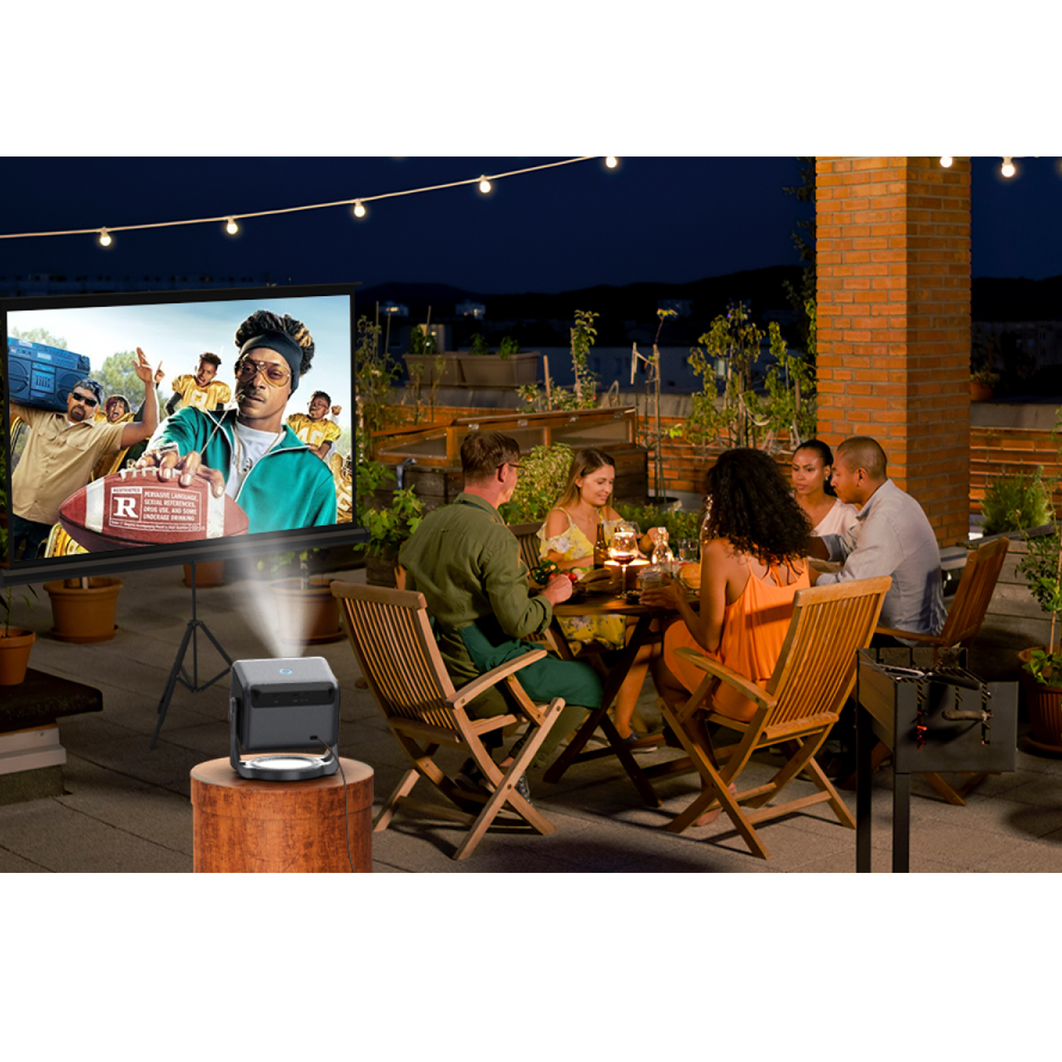 People enjoy an outdoor movie night with a projector and dinner at a table.