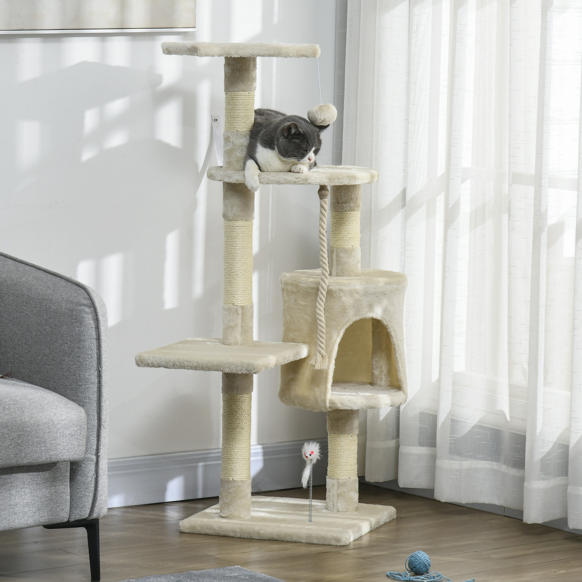 Un gatto riposa su un tiragraffi con giocattoli, accanto a una poltrona.
