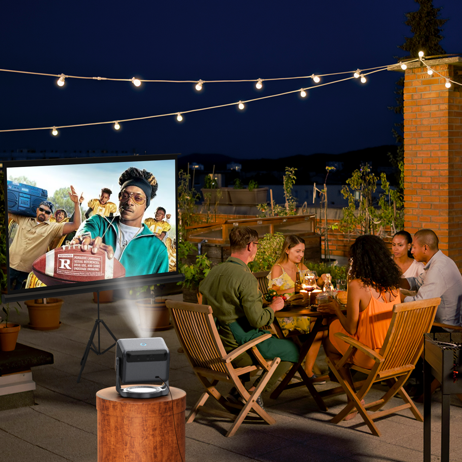 People dine outdoors at night as a projector displays a movie on a screen.