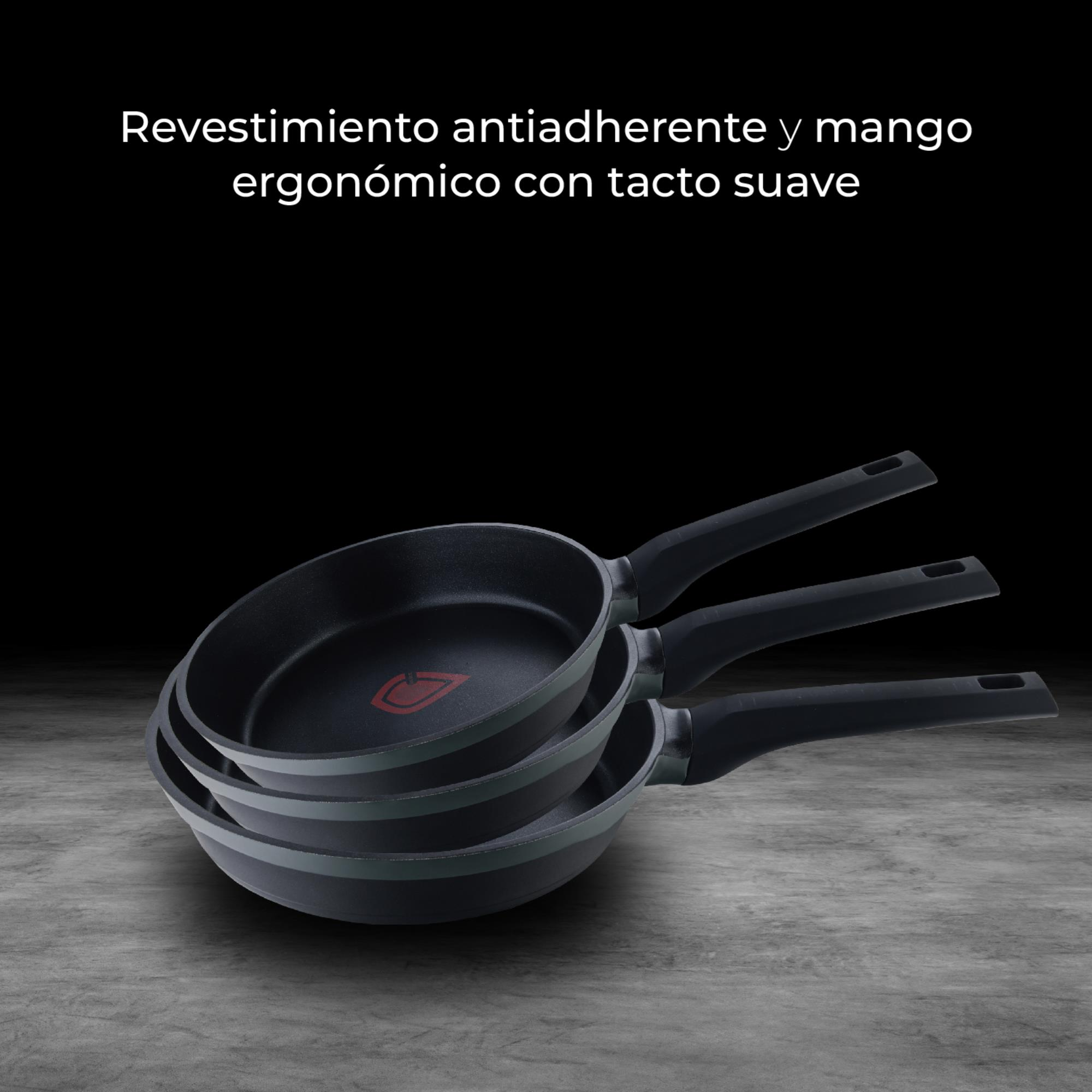 Tres sartenes negras con logos rojos, apiladas sobre hormigón.