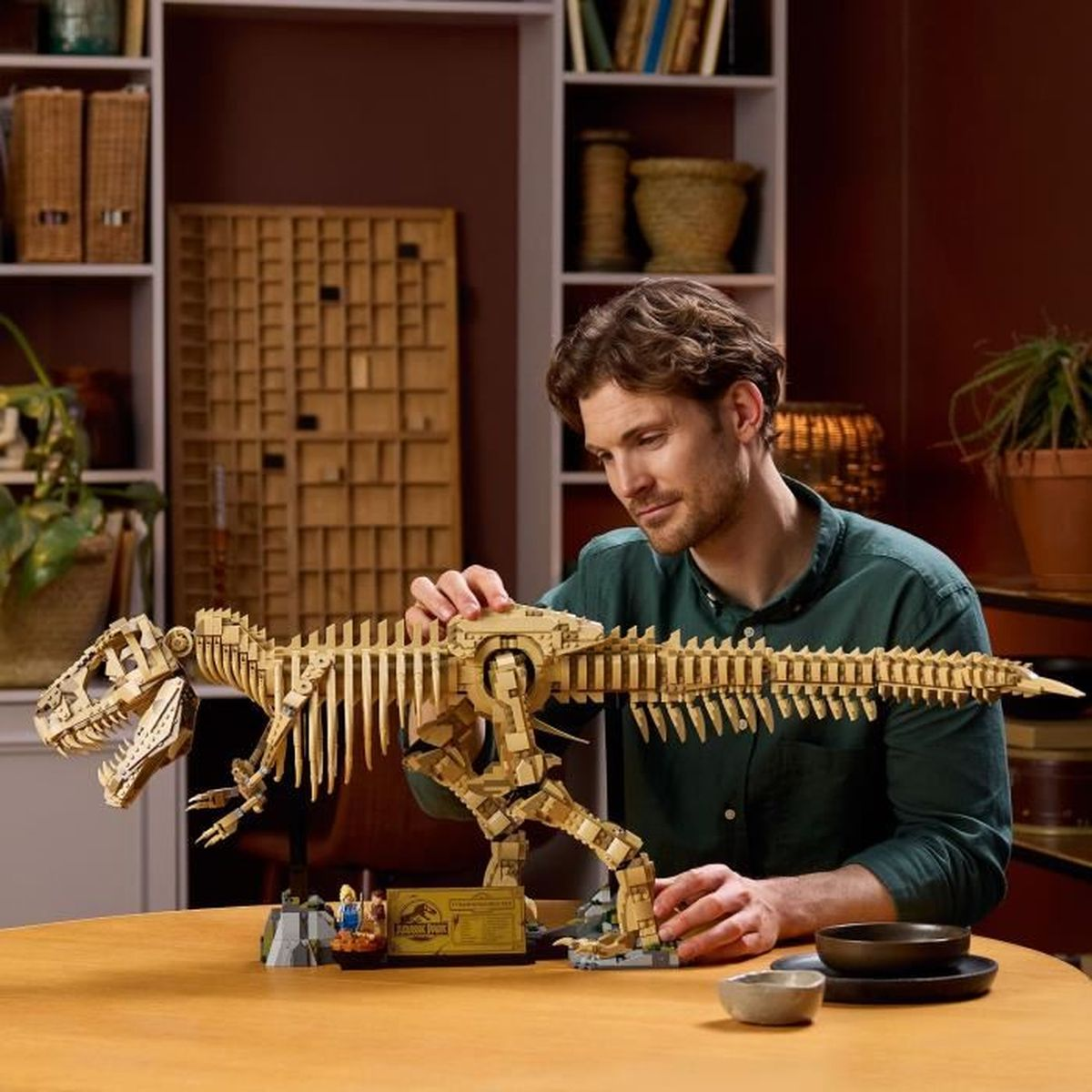 Mężczyzna ogląda drewniany model szkieletu Tyrannosaurusa Rexa na stole.