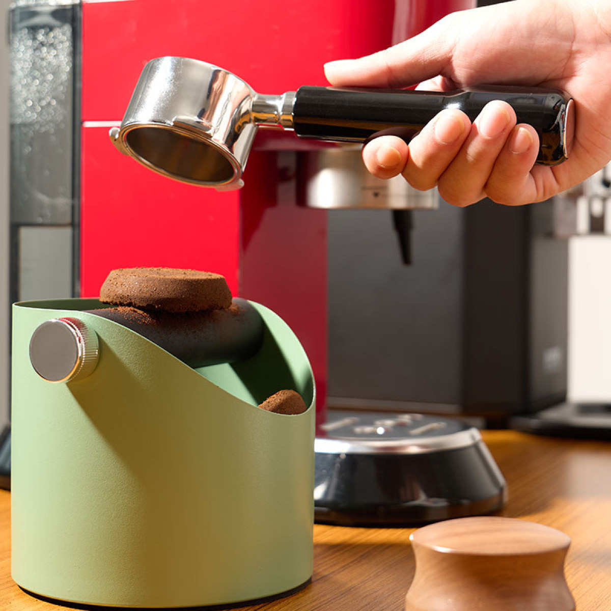 Eine Hand hält einen Siebträger über einen grünen Kaffeesatzbehälter.