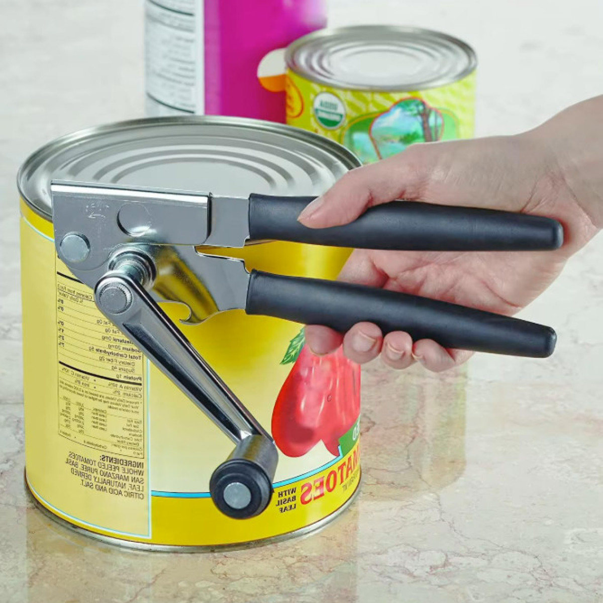 Eine Hand benutzt einen Dosenöffner, um eine gelbe Tomatendose zu öffnen.