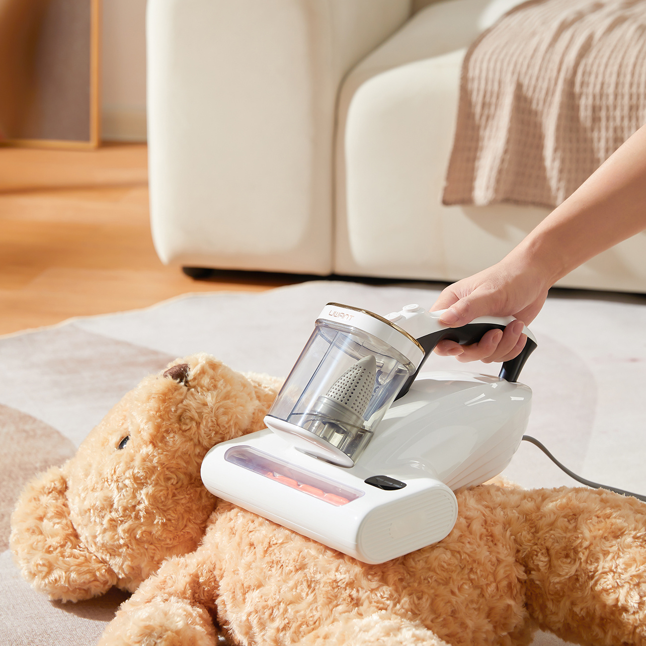 Ręka trzyma biały odkurzacz czyszczący pluszowego misia na dywanie.