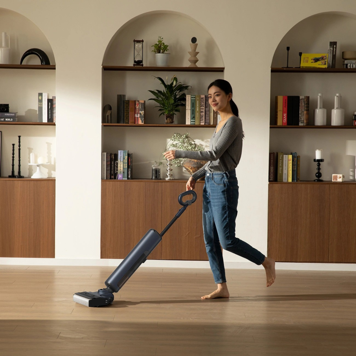 Kobieta w dżinsach myje drewnianą podłogę niebieskim mopem.