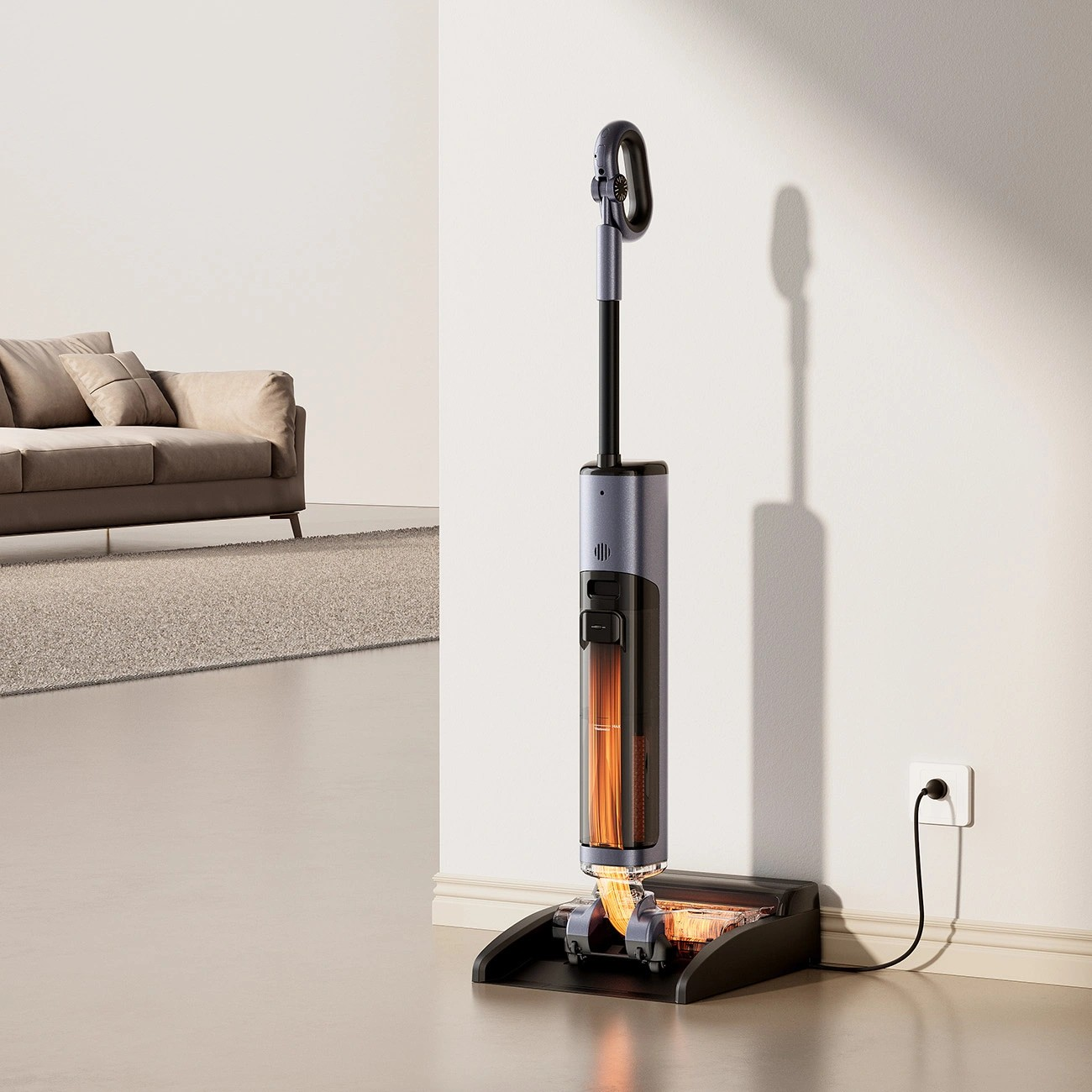 Szary odkurzacz z pomarańczowym światłem w podstawie stoi przy ścianie.