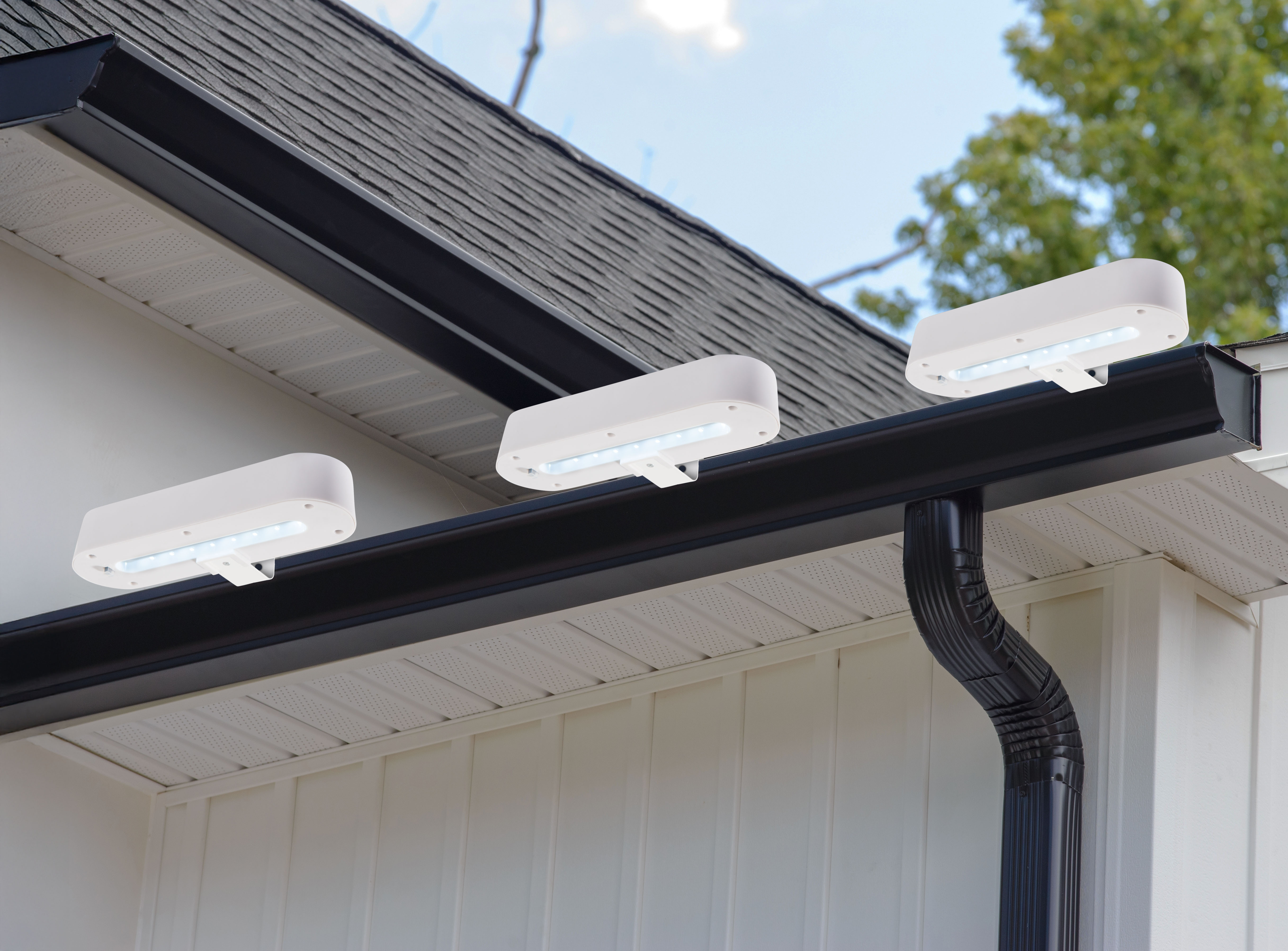 Drei weiße LED-Außenleuchten sind an der Regenrinne eines Hauses montiert.