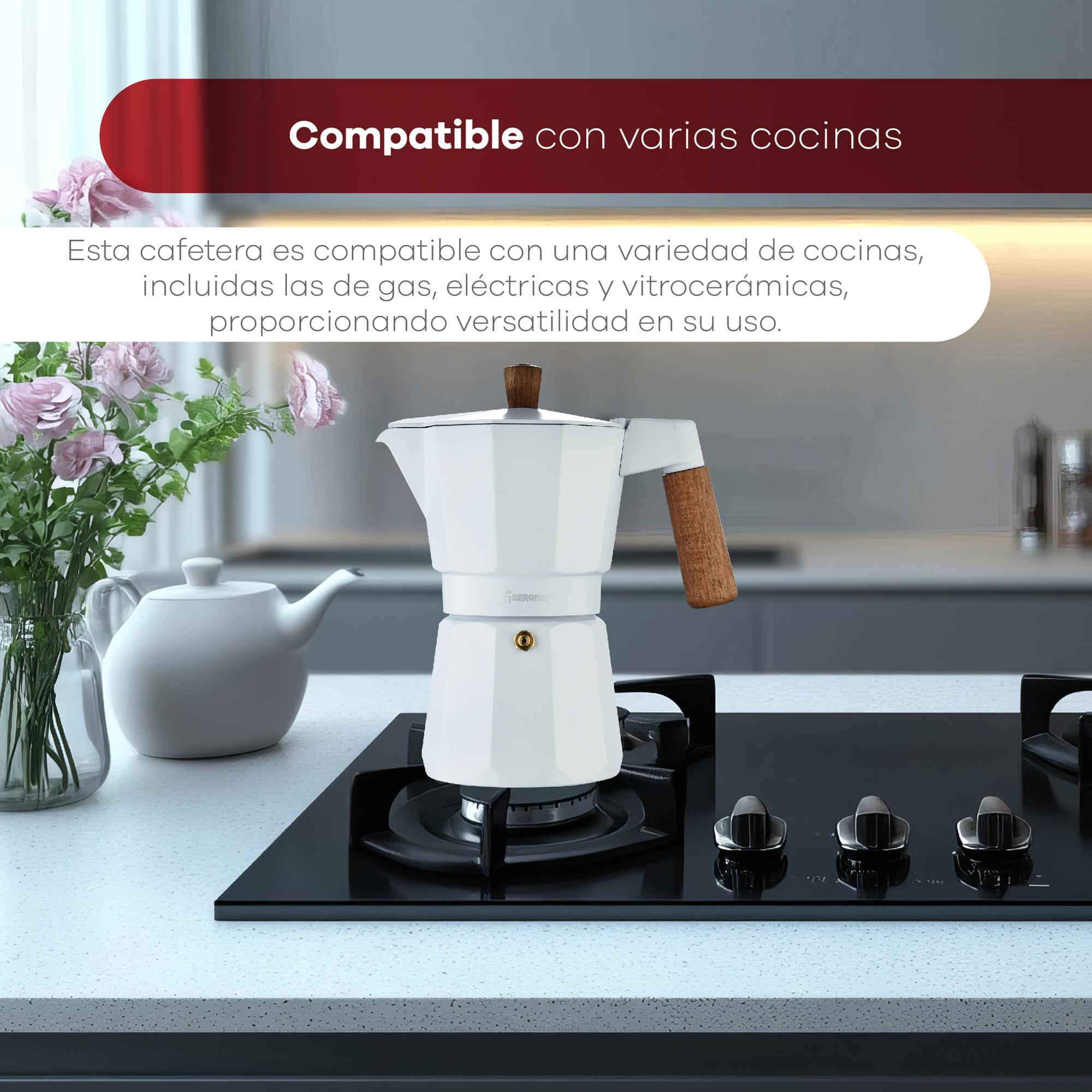 Una cafetera blanca sobre una cocina de gas negra. Flores en primer plano.