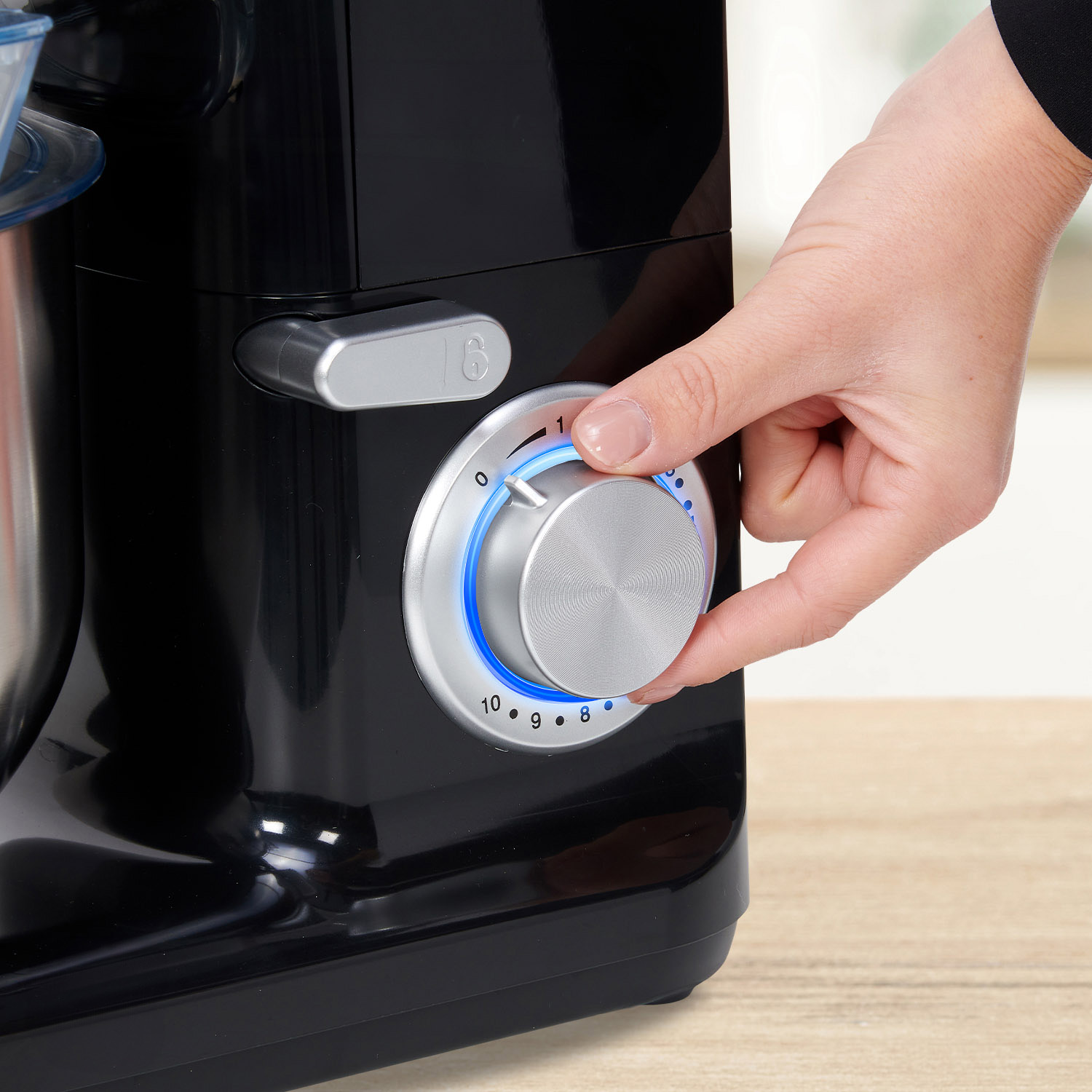 A hand turns the silver dial on a black kitchen mixer.