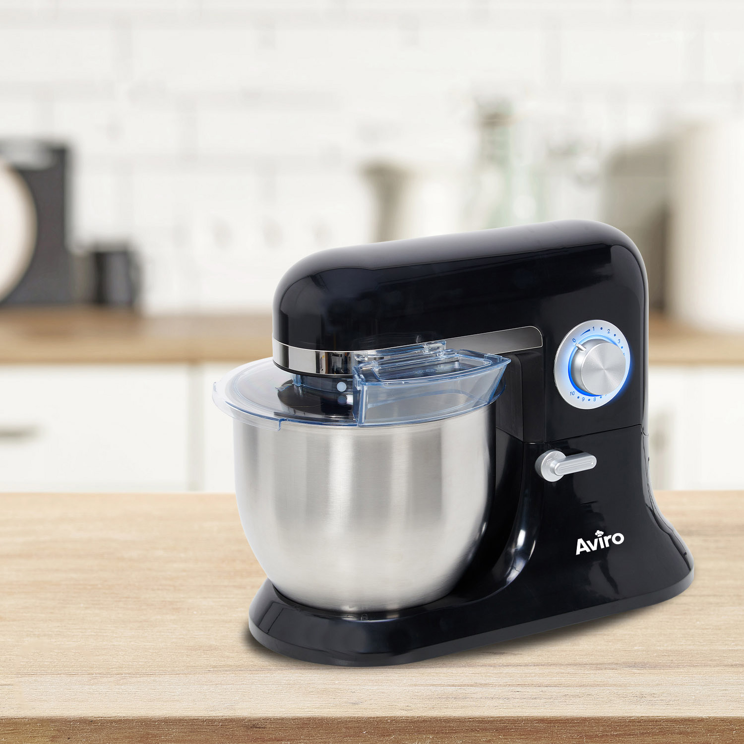 A black Avrio stand mixer with a silver bowl sits on a wooden table in a kitchen.