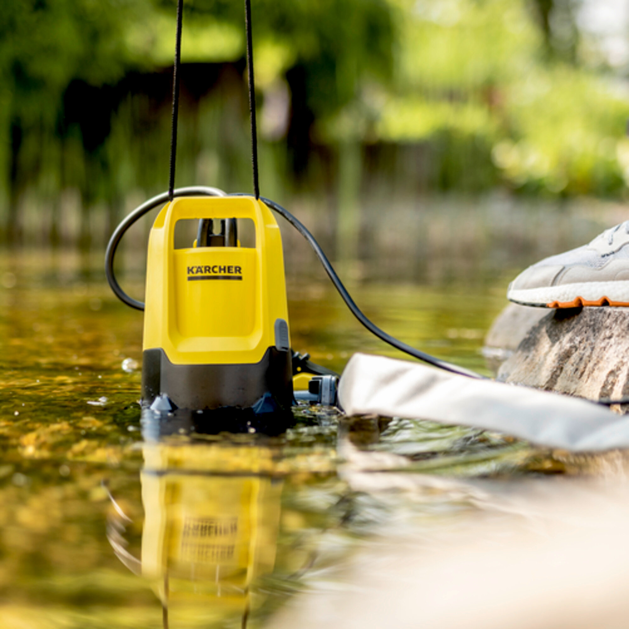 Żółta pompa zanurzeniowa Kärcher stoi w wodzie obok kamienia.