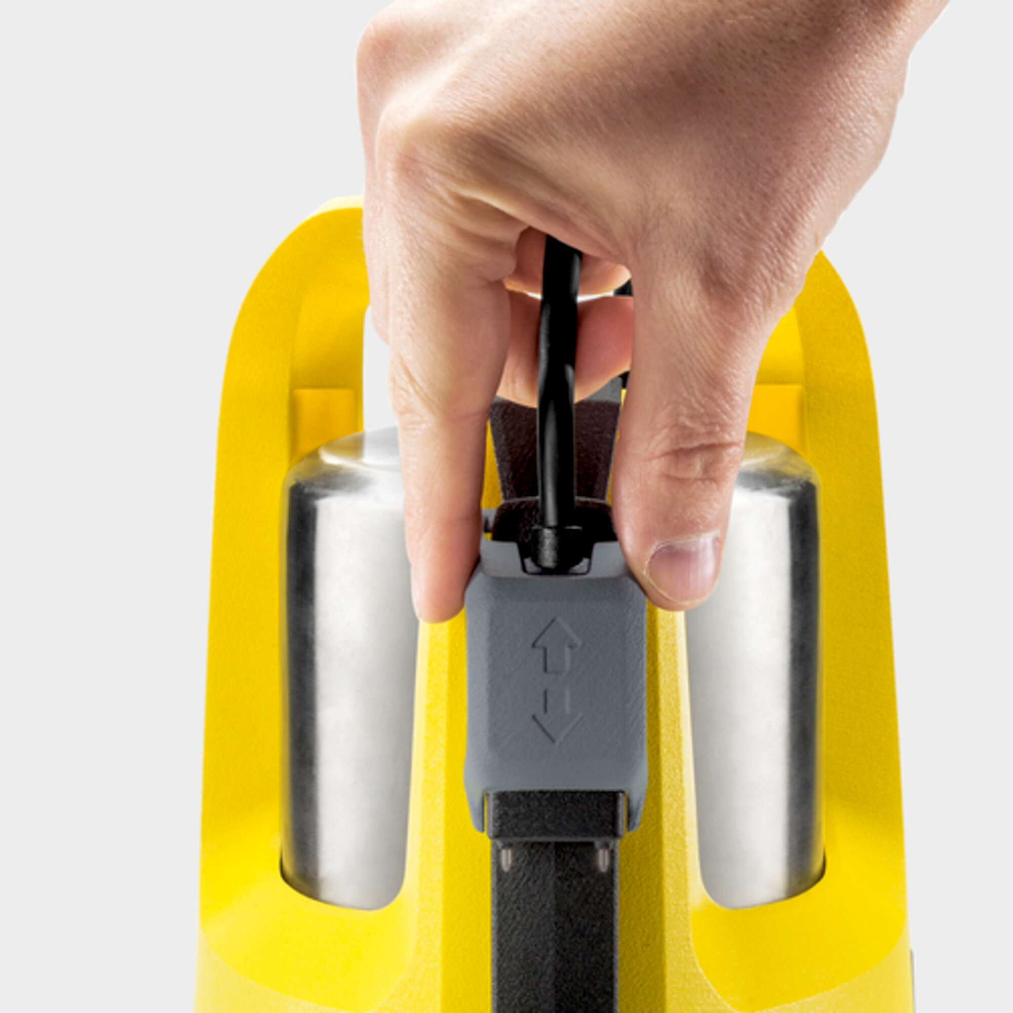 Ręka trzyma kabel przy żółtym urządzeniu z srebrnymi cylindrami.