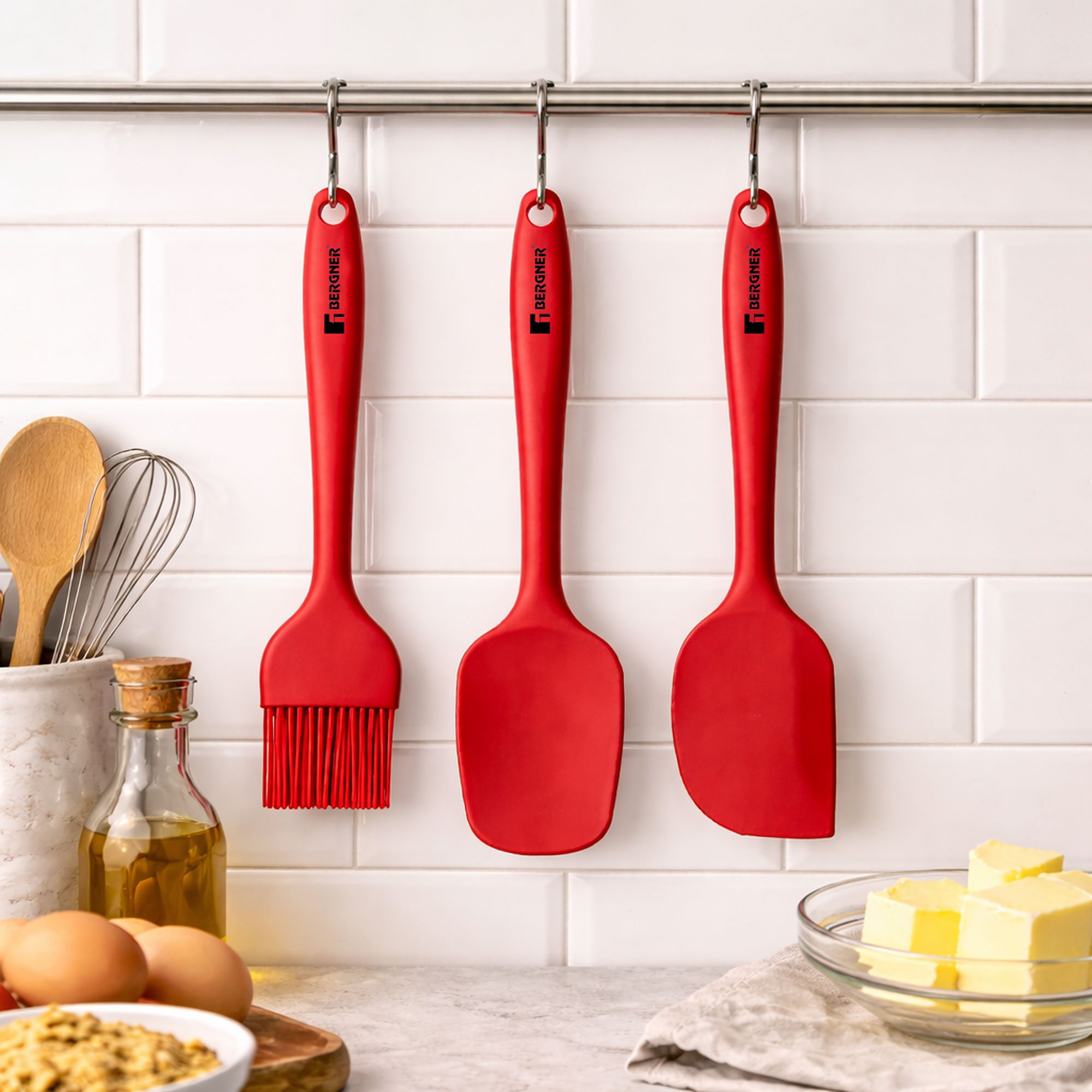 Tres utensilios de cocina rojos cuelgan de una barra frente a azulejos blancos.