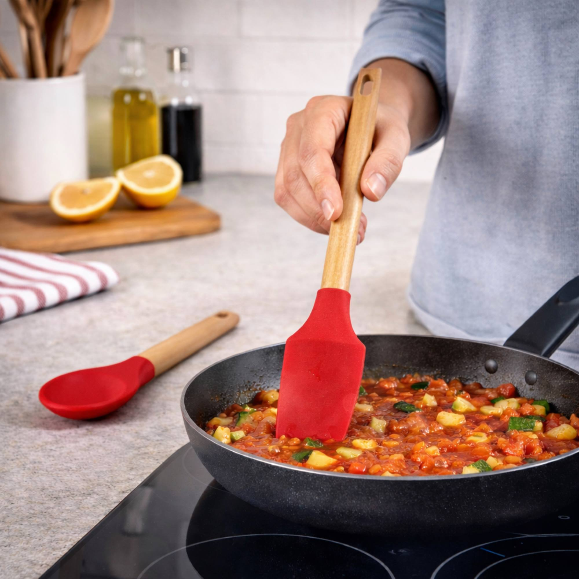 Una espátula roja de silicona revuelve verduras en una sartén en la estufa.