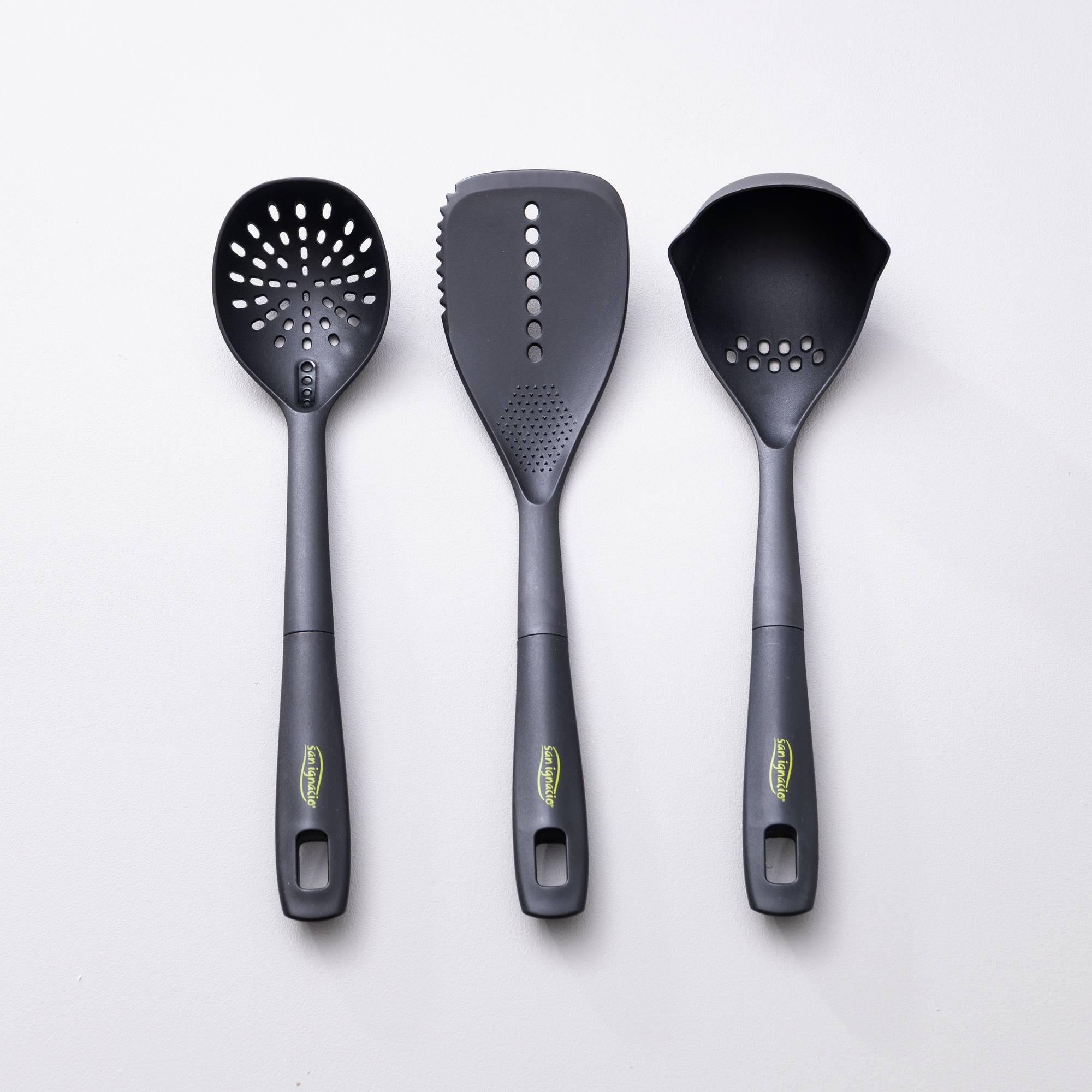 Tres utensilios de cocina negros con agujeros y mangos.
