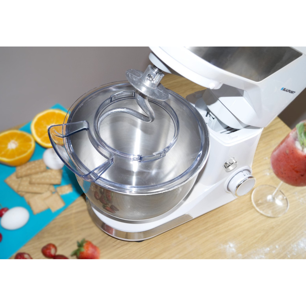 Un robot da cucina bianco con ciotola in acciaio inox, accanto a arance, uova e cracker.
