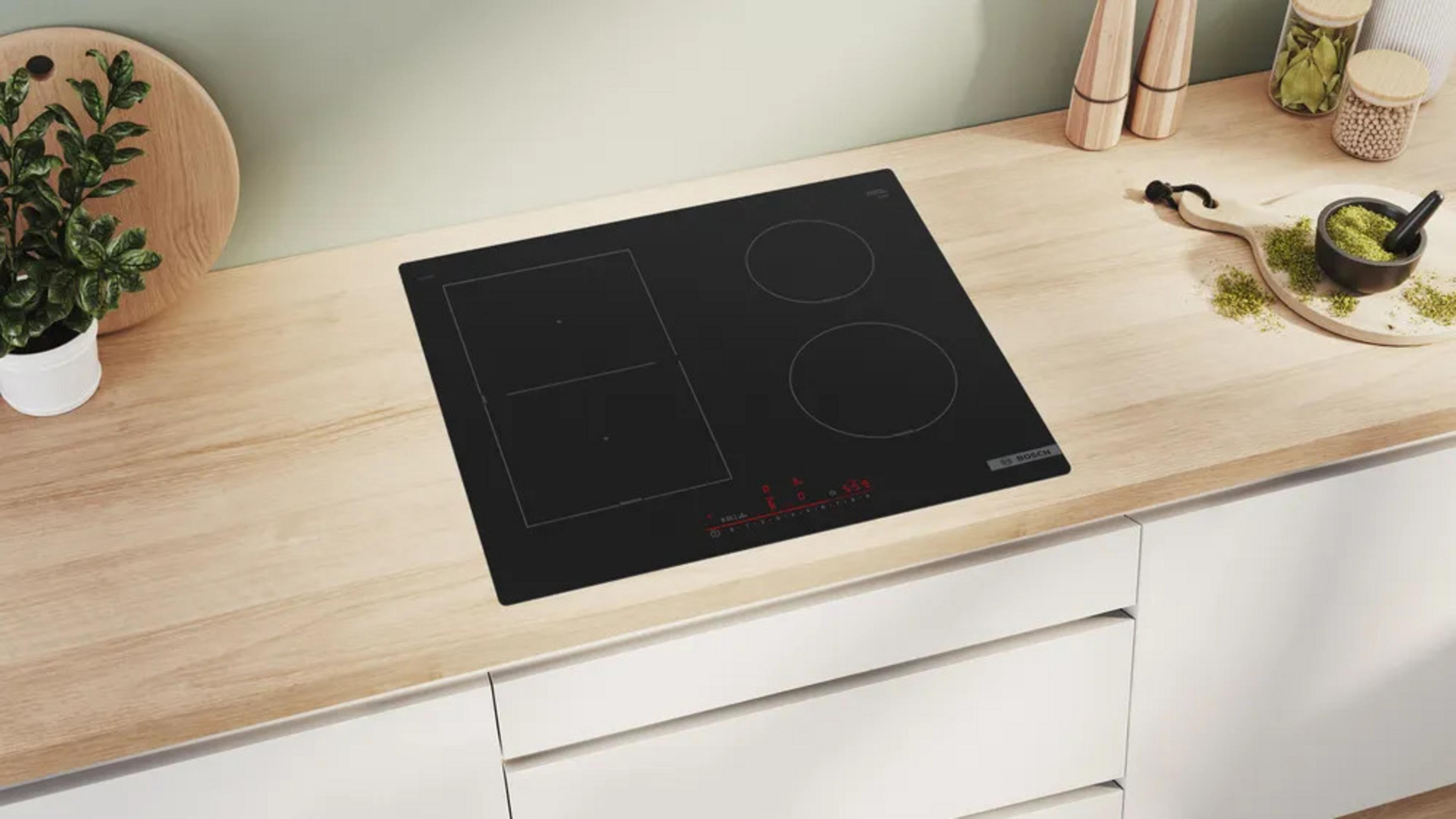 Un piano cottura a induzione nero su un piano di lavoro in legno con utensili da cucina.