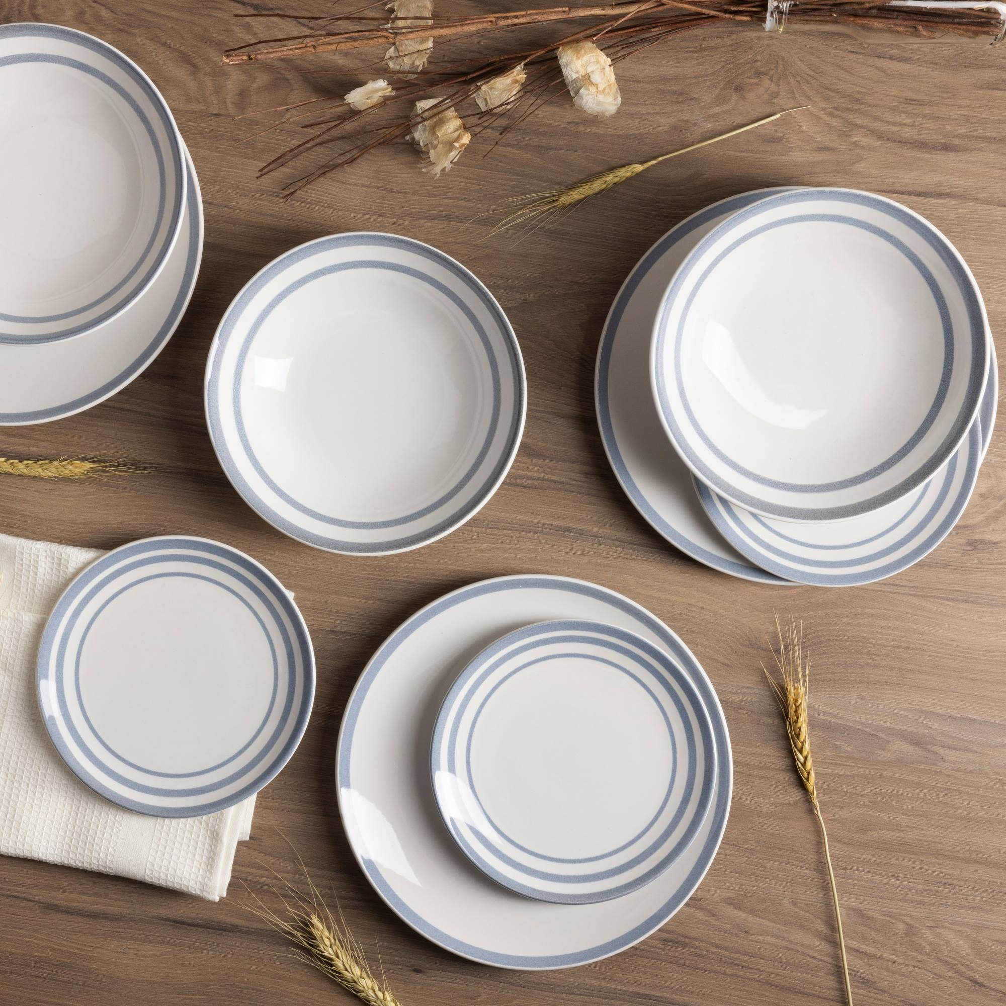 Platos blancos con anillos azules sobre mesa de madera, decorados con ramas.