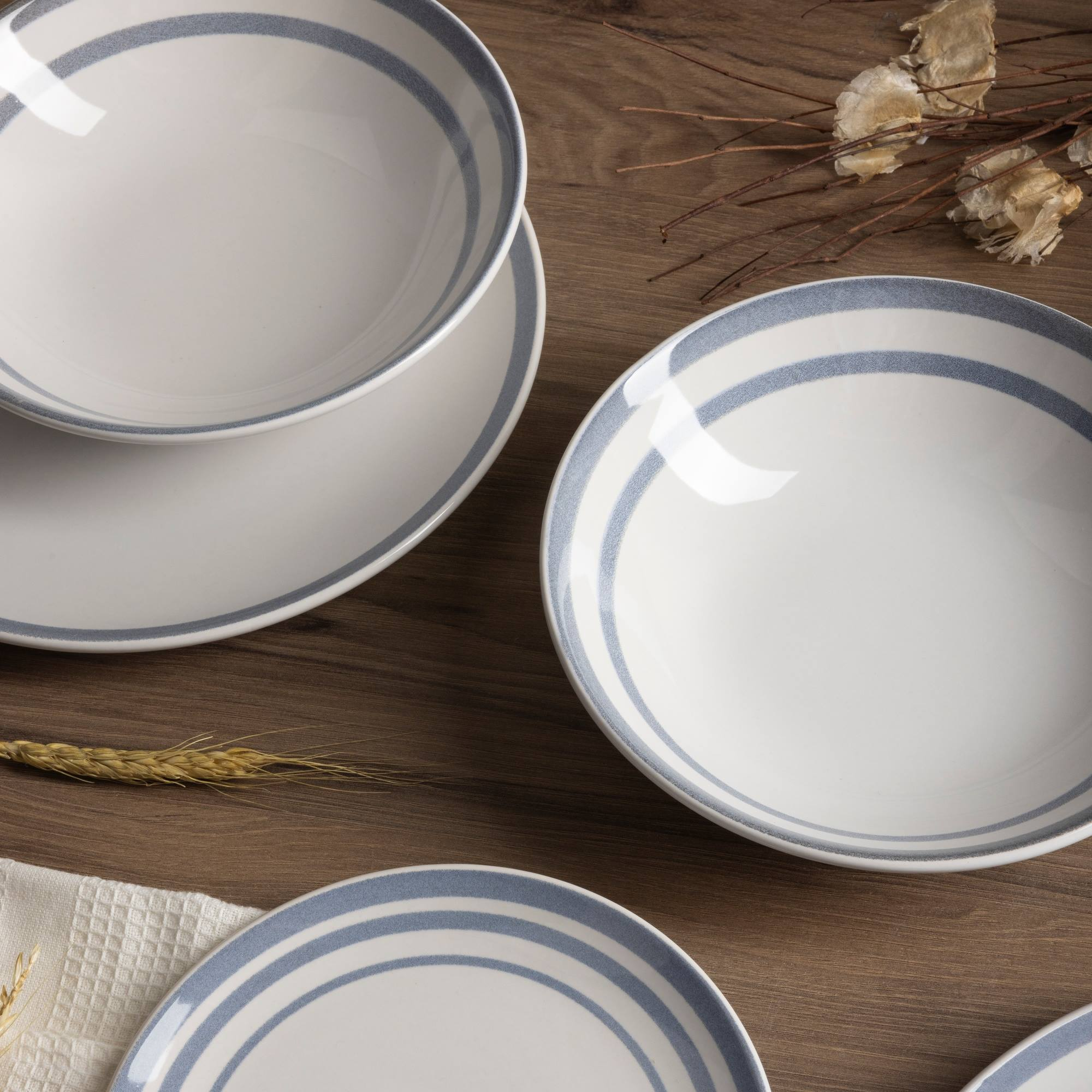 Cuencos y platos blancos con rayas azules sobre mesa de madera.