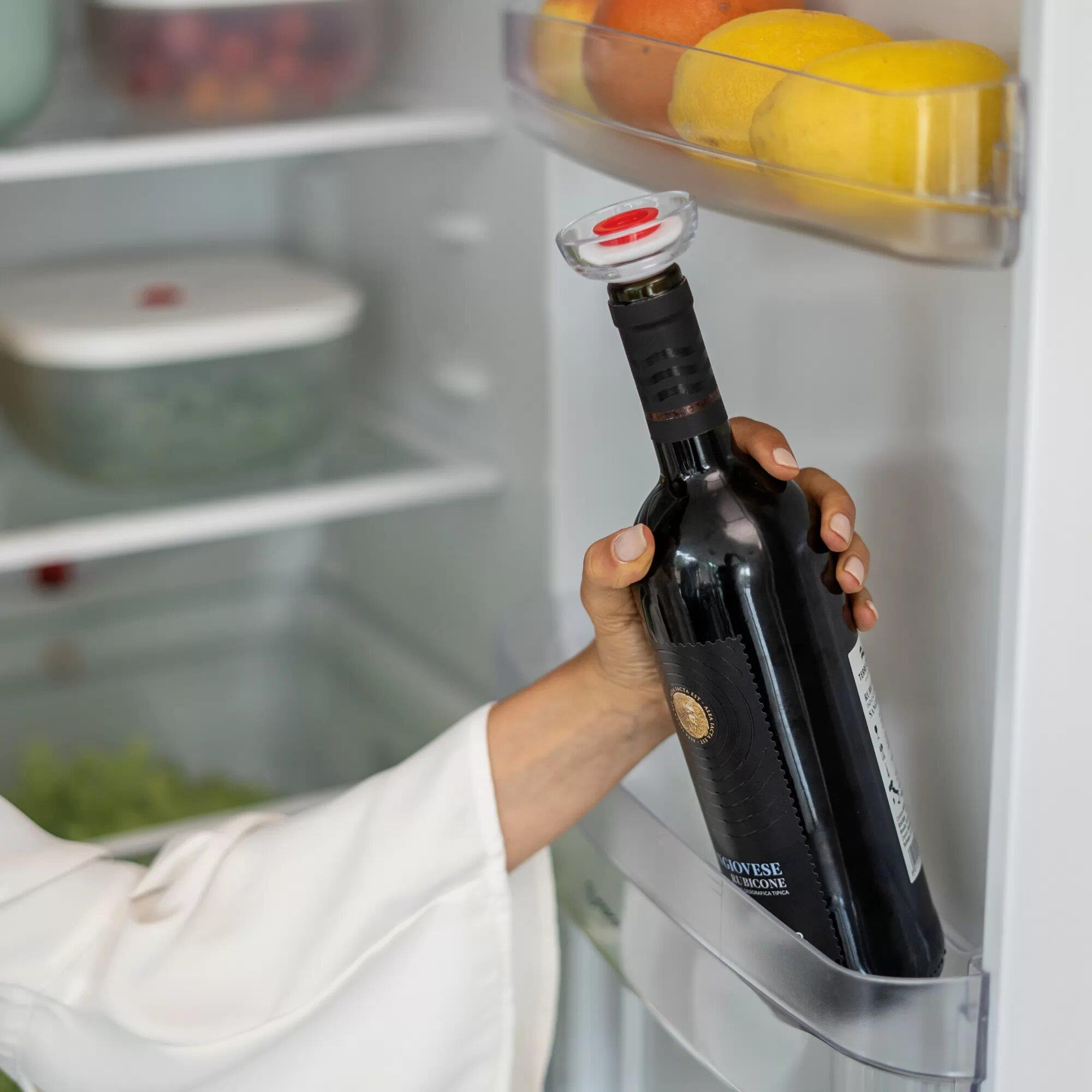 Una mano sosteniendo una botella de vino tinto con tapón dentro de un refrigerador.
