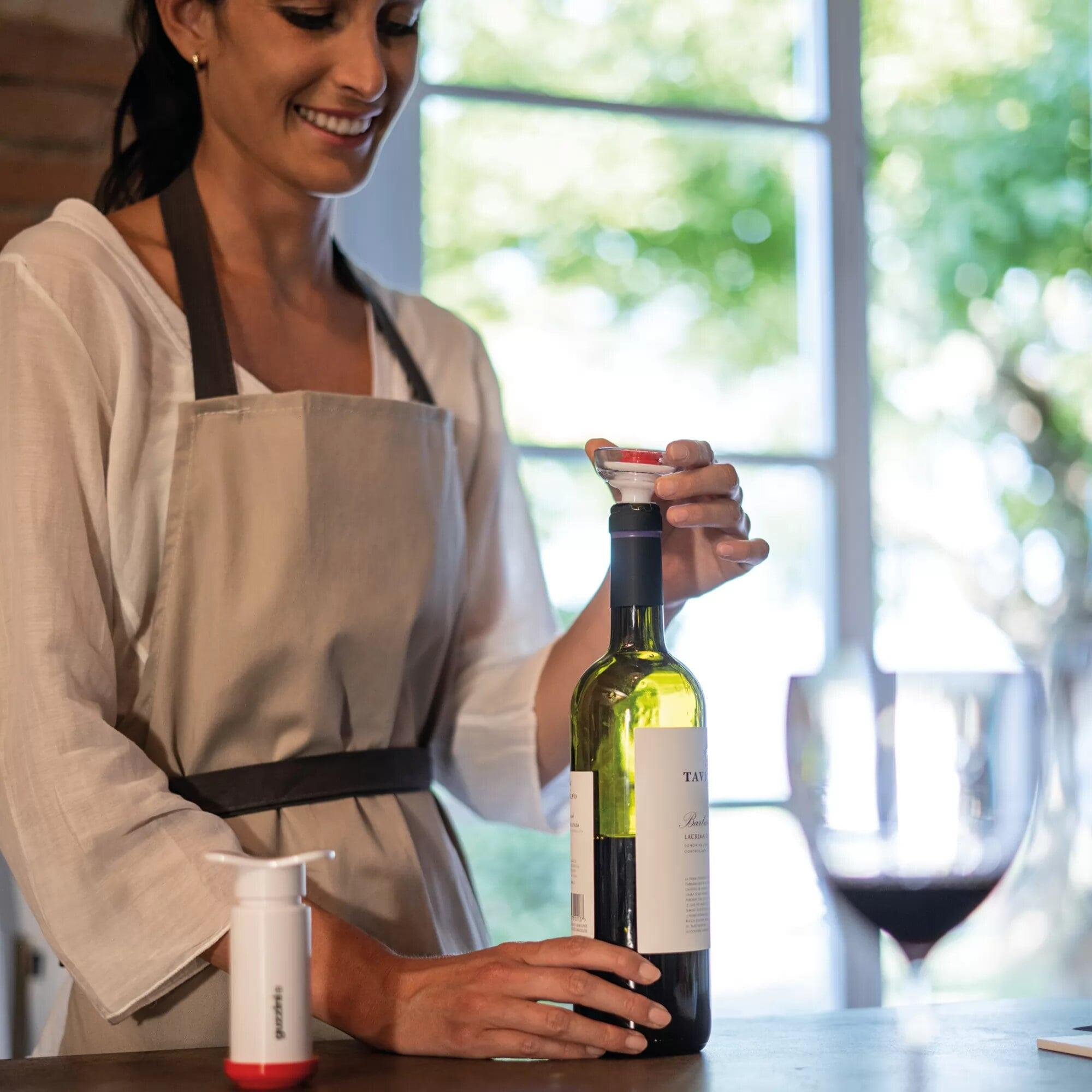 Una mujer con delantal usa un sacacorchos en una botella de vino.