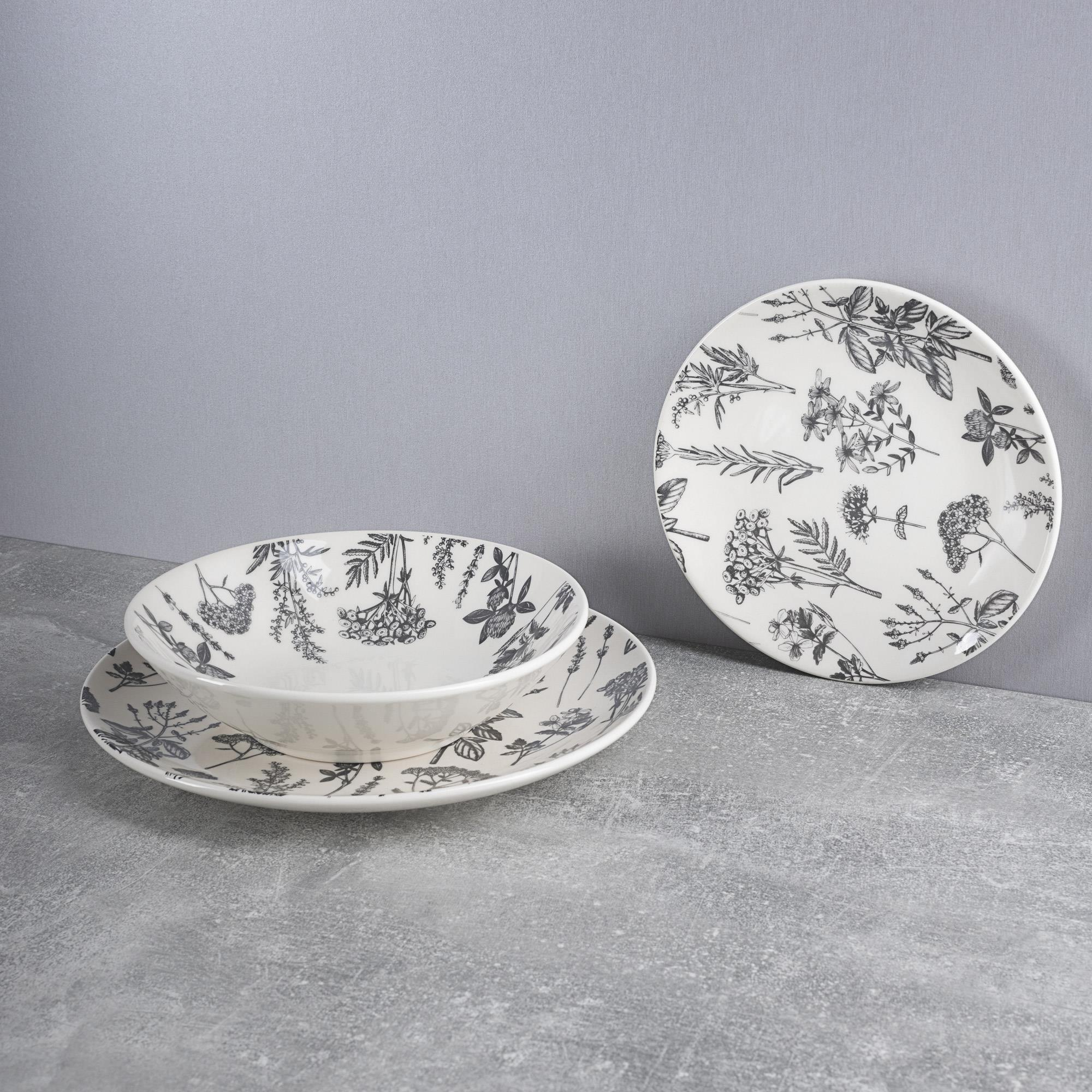Platos y cuenco blancos con motivos botánicos sobre fondo gris.