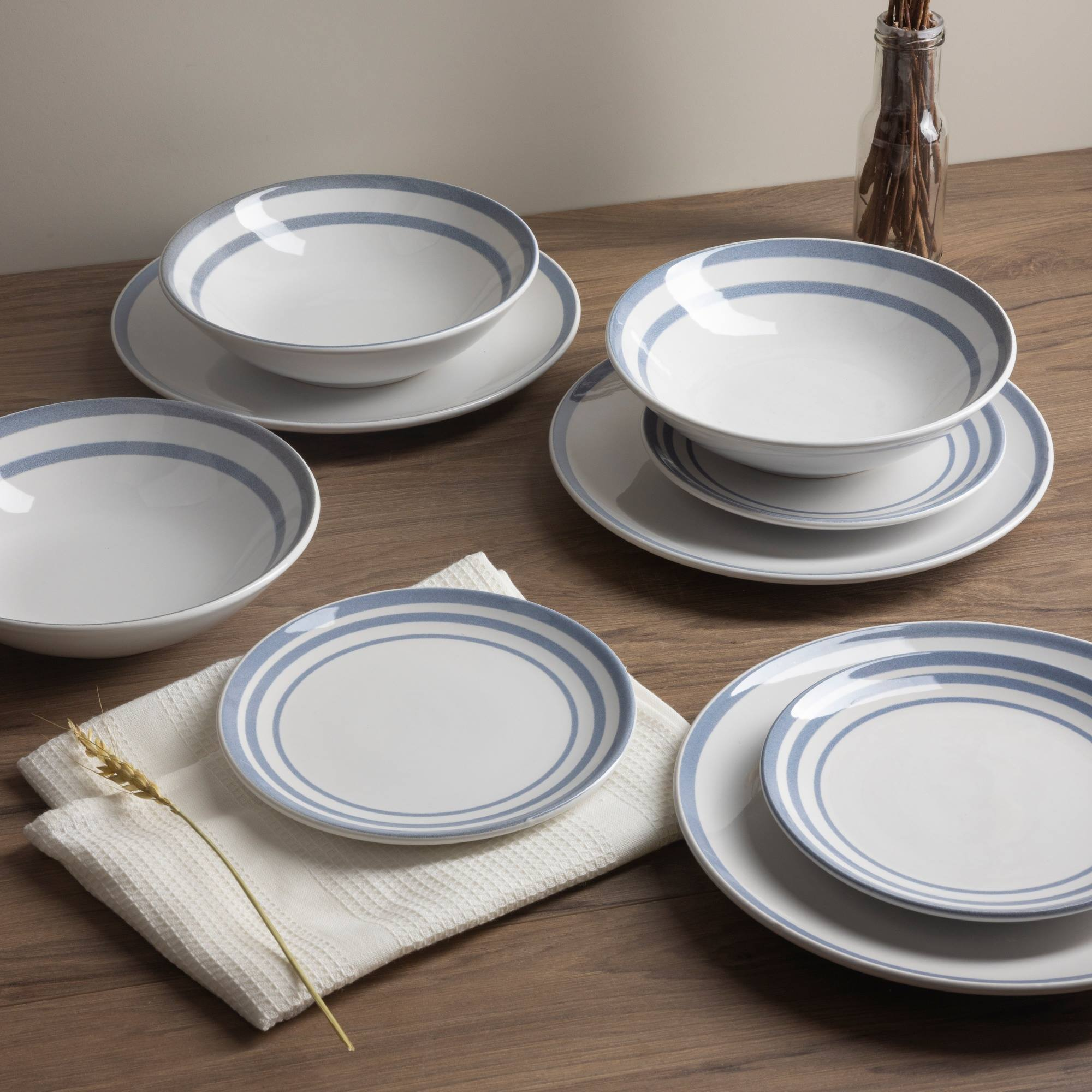 Platos y cuencos blancos con rayas azules sobre mesa de madera. Espiga de trigo sobre paño.