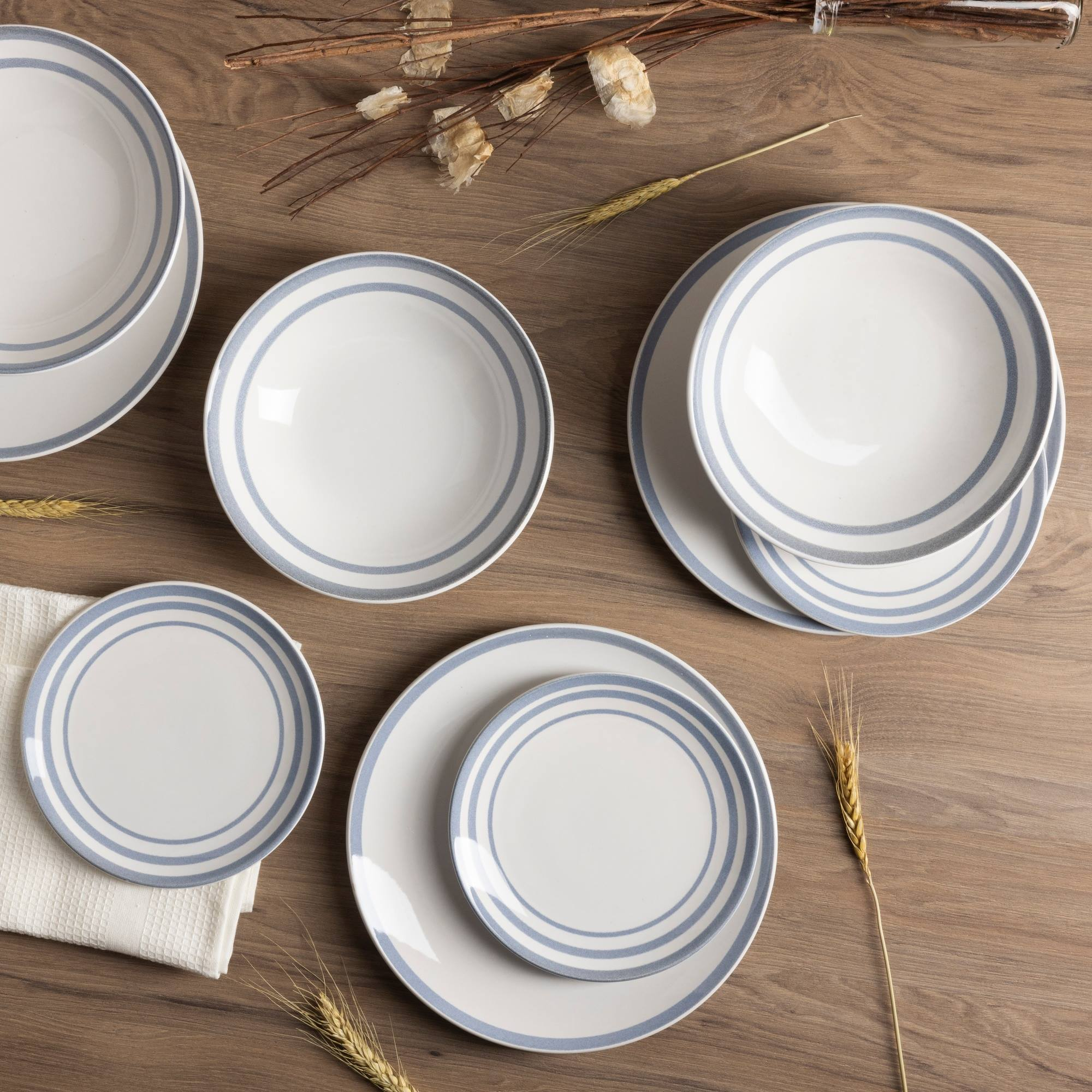 Platos blancos con rayas azules sobre mesa de madera con decoración.